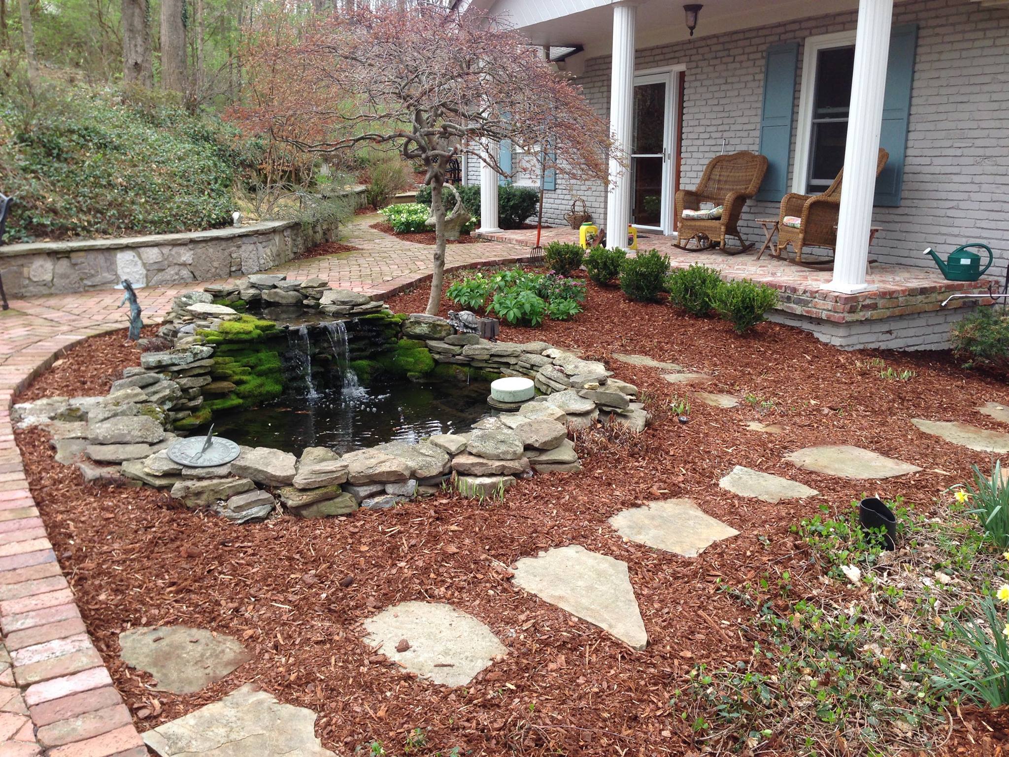 Landscaping with mulch, stone path, and small pond
