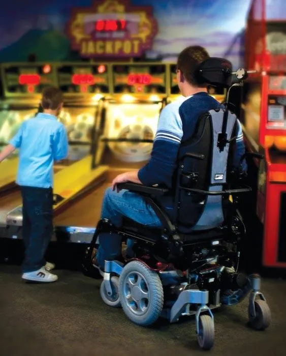 Person in power wheelchair enjoying a game with child at an arcade, showcasing mobility independence and engagement in recreational activities.