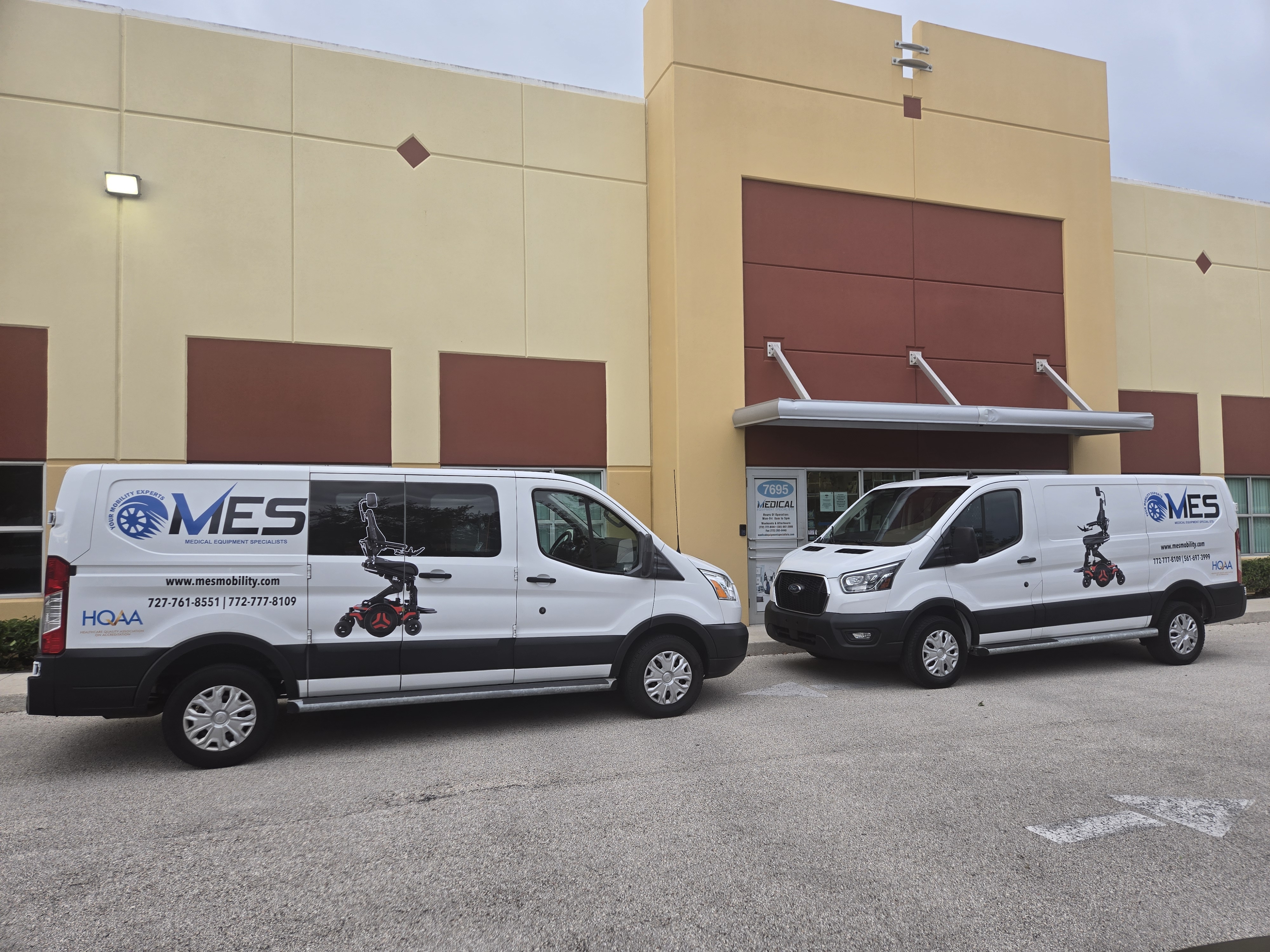 Two MES Mobility vans parked outside a medical equipment facility, featuring the MES logo and a graphic of a power wheelchair, emphasizing their mobility solutions and services in Florida.