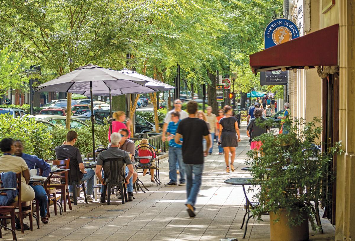 Downtown Greenville Main Street with tree-lined sidewalks, outdoor cafes, and pedestrians