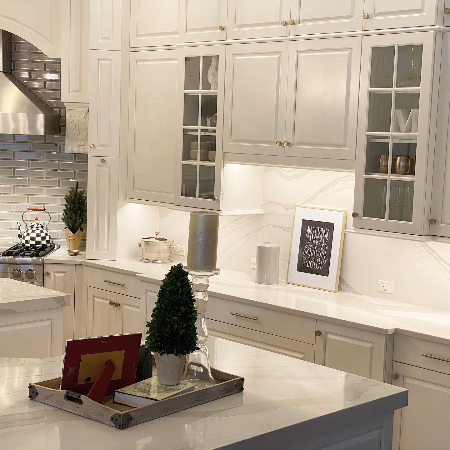 Modern kitchen with white cabinetry, stainless steel appliances, marble countertops, decorative plants, and a framed inspirational quote, showcasing a stylish home improvement project by Diamond Pro Finishes.