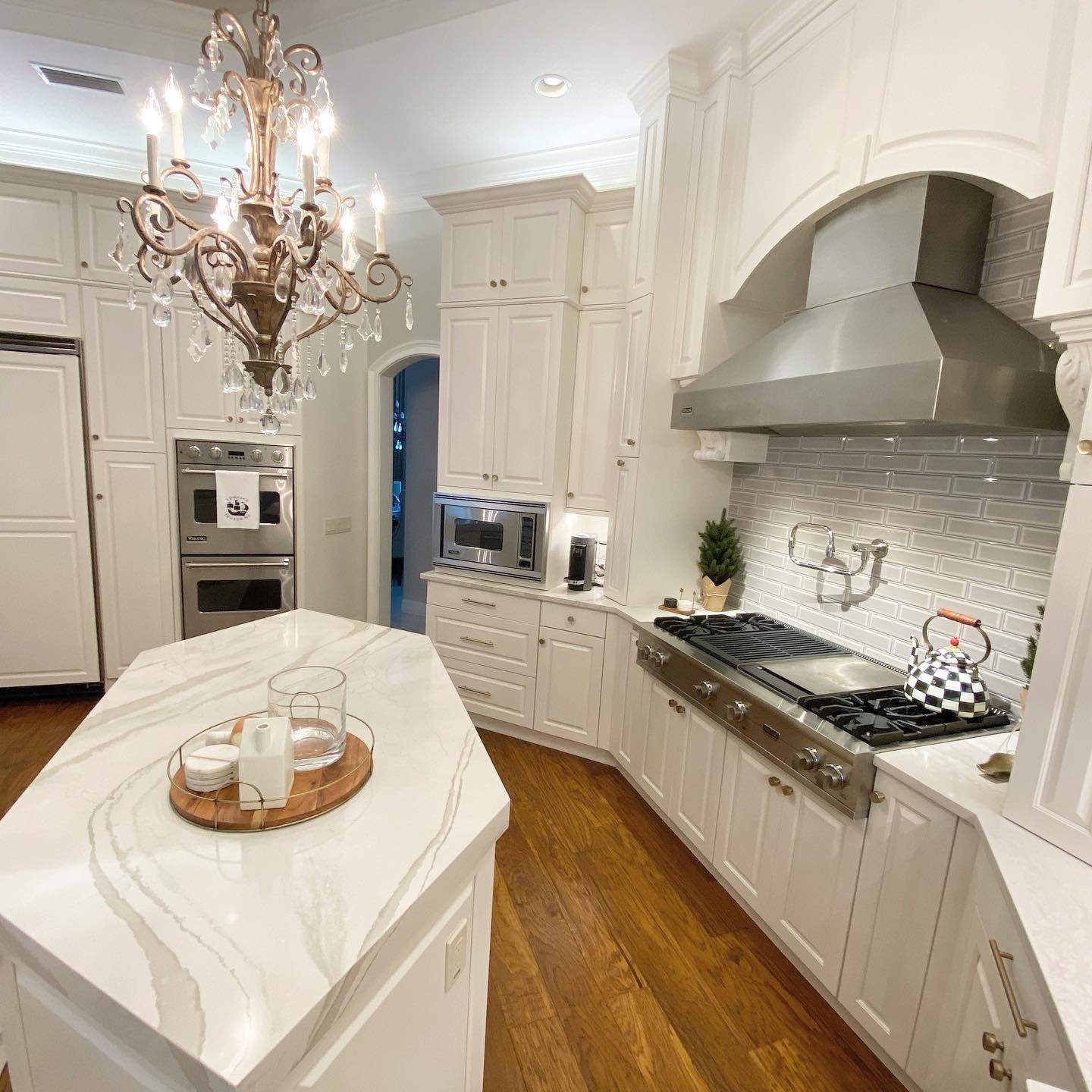 Modern kitchen featuring white cabinetry, stainless steel appliances, marble countertop, and elegant chandelier, showcasing a stylish home transformation by Diamond Pro Finishes.