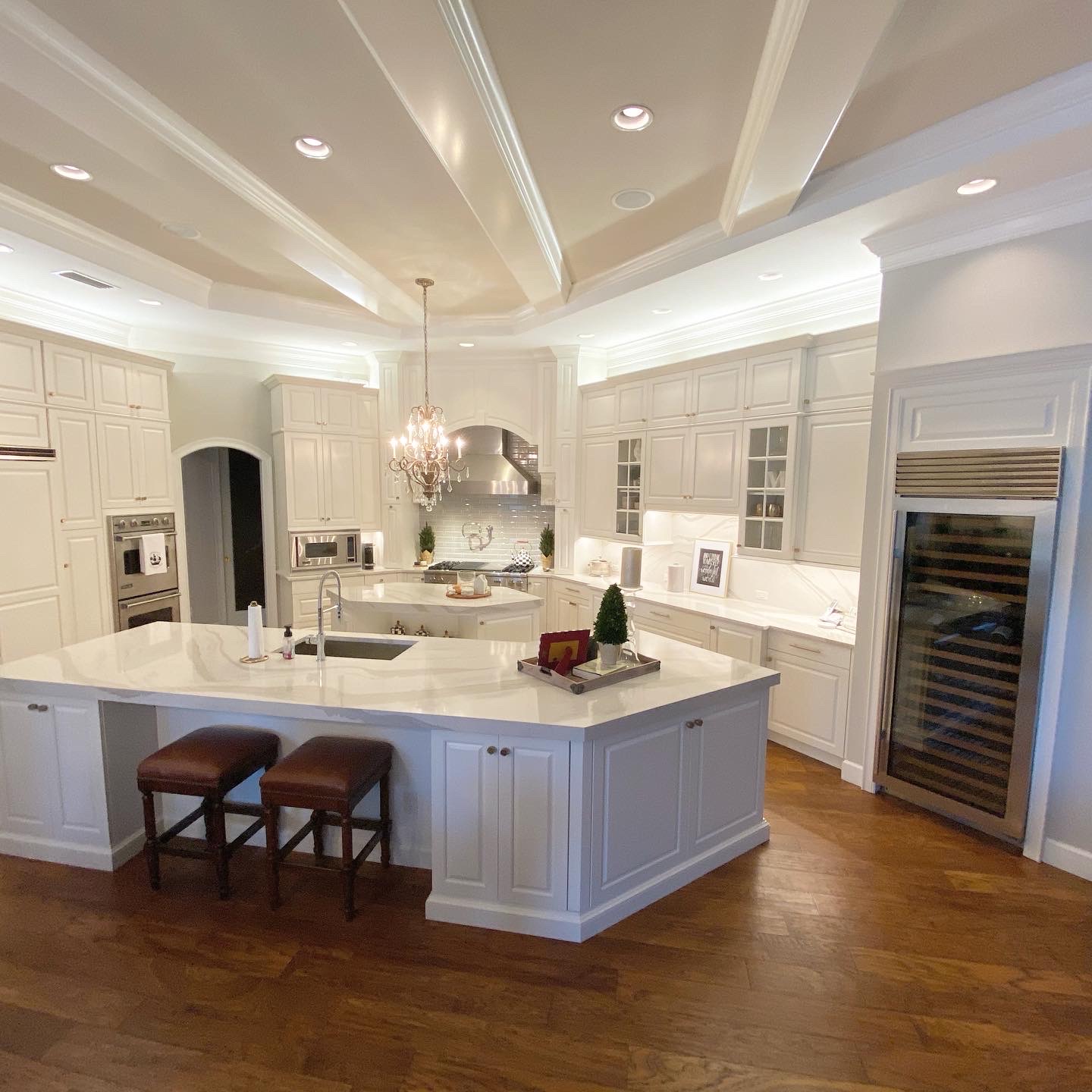 Modern kitchen featuring white cabinetry, marble countertops, and elegant chandelier, showcasing a spacious layout ideal for home remodeling and improvement services.