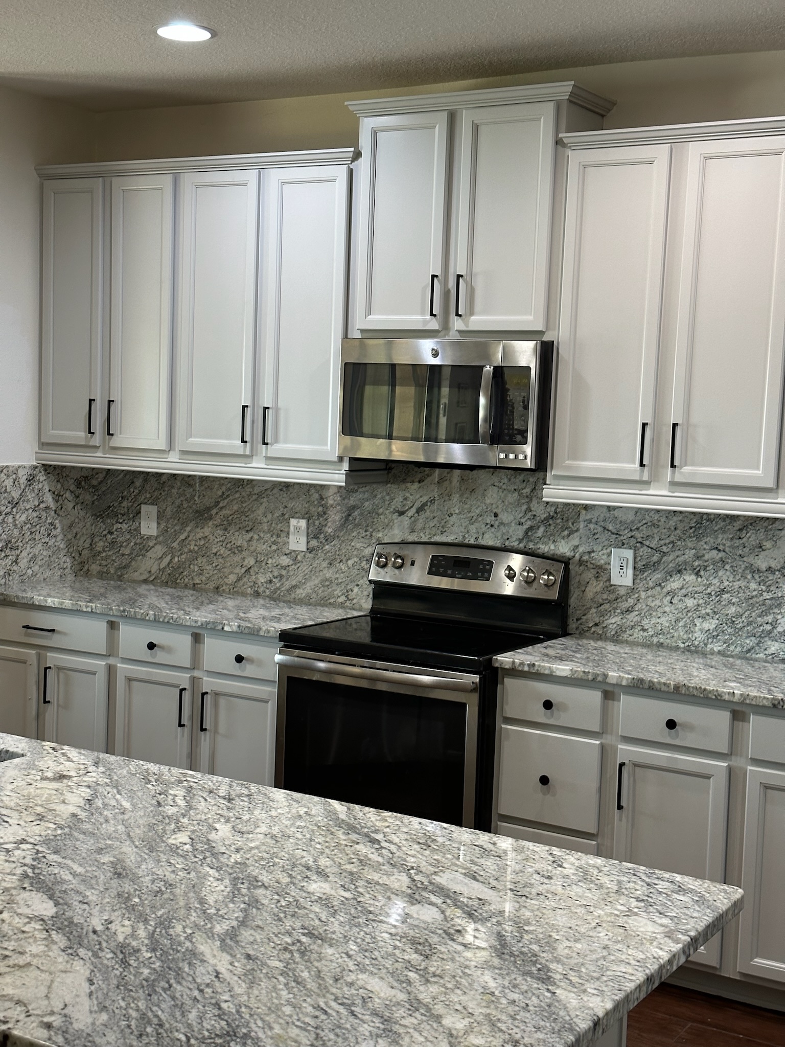 Modern kitchen featuring freshly refinished white cabinets, stainless steel appliances, and granite countertops, illustrating the benefits of professional cabinet refinishing services by Diamond Pro Finishes.