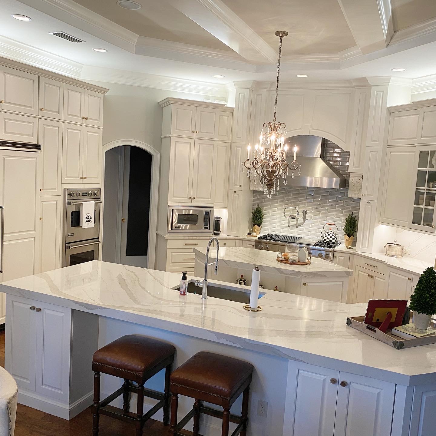 Modern kitchen featuring white cabinetry, elegant chandelier, marble countertops, stainless steel appliances, and decorative plants, showcasing a recent home transformation by Diamond Pro Finishes.