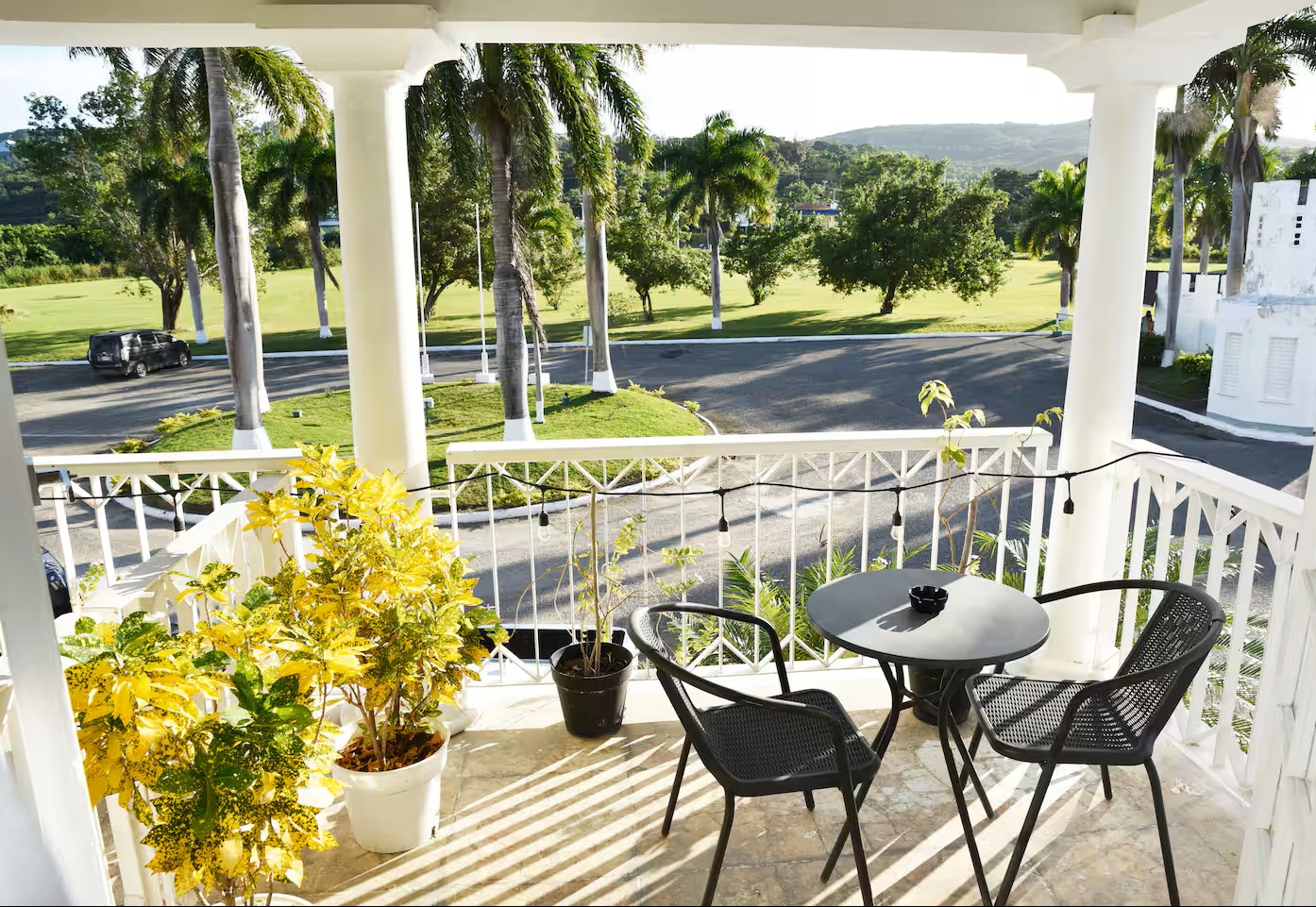 Sunlit Balcony Bistro Table with Potted Tropical Flora & Estate Grounds View