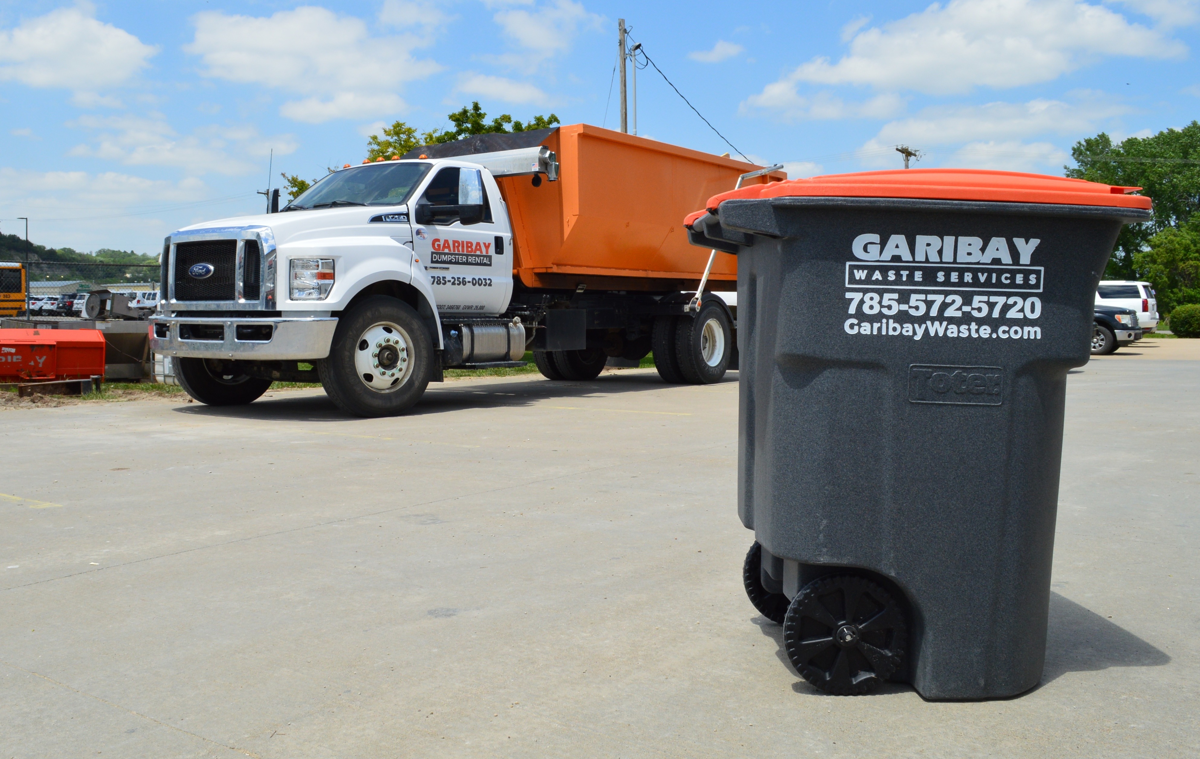 White truck with orange roll-off dumpster and a trash bin