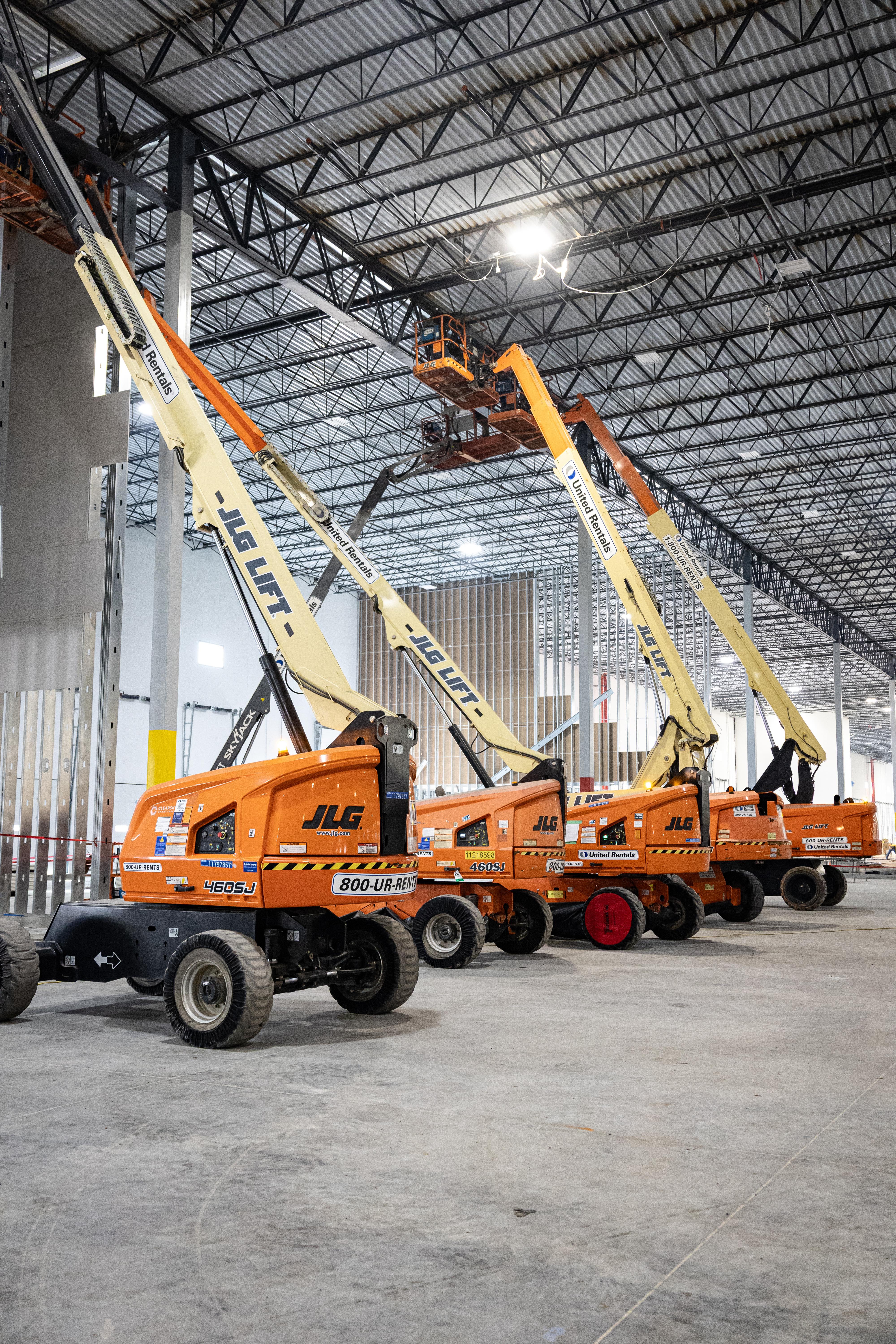 Multiple JLG boom lifts inside a large industrial warehouse construction site