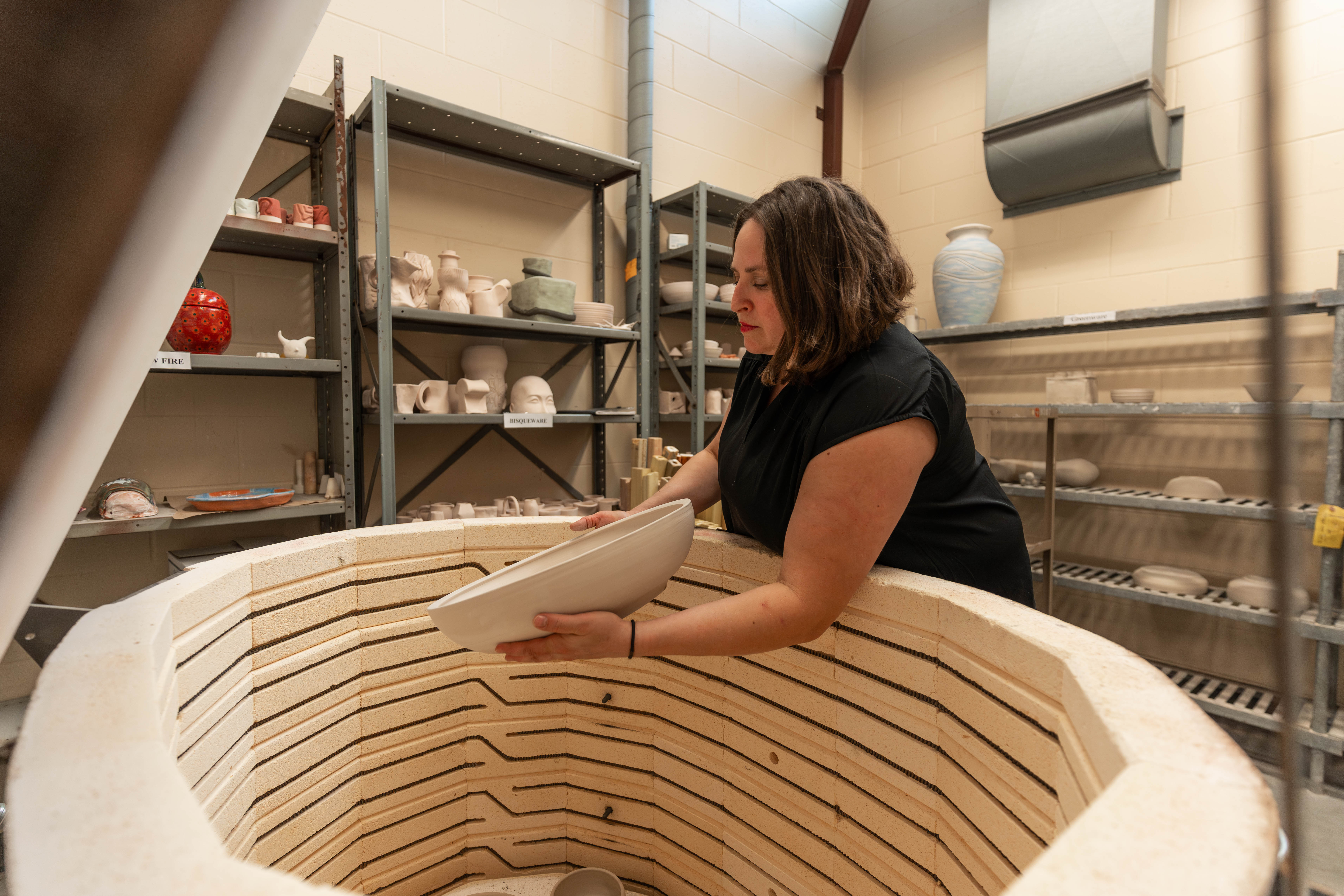 Instructor loading ceramic work into a large kiln during studio training session