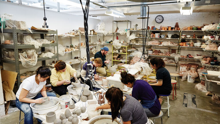 Students working at pottery wheels in a busy ceramic studio classroom
