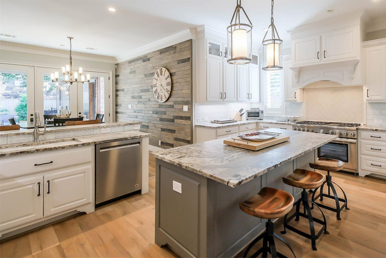 Modern kitchen with granite countertops, stainless steel appliances, and a rustic wood accent wall, showcasing a spacious layout ideal for Texas country homes in Fort Bend County.