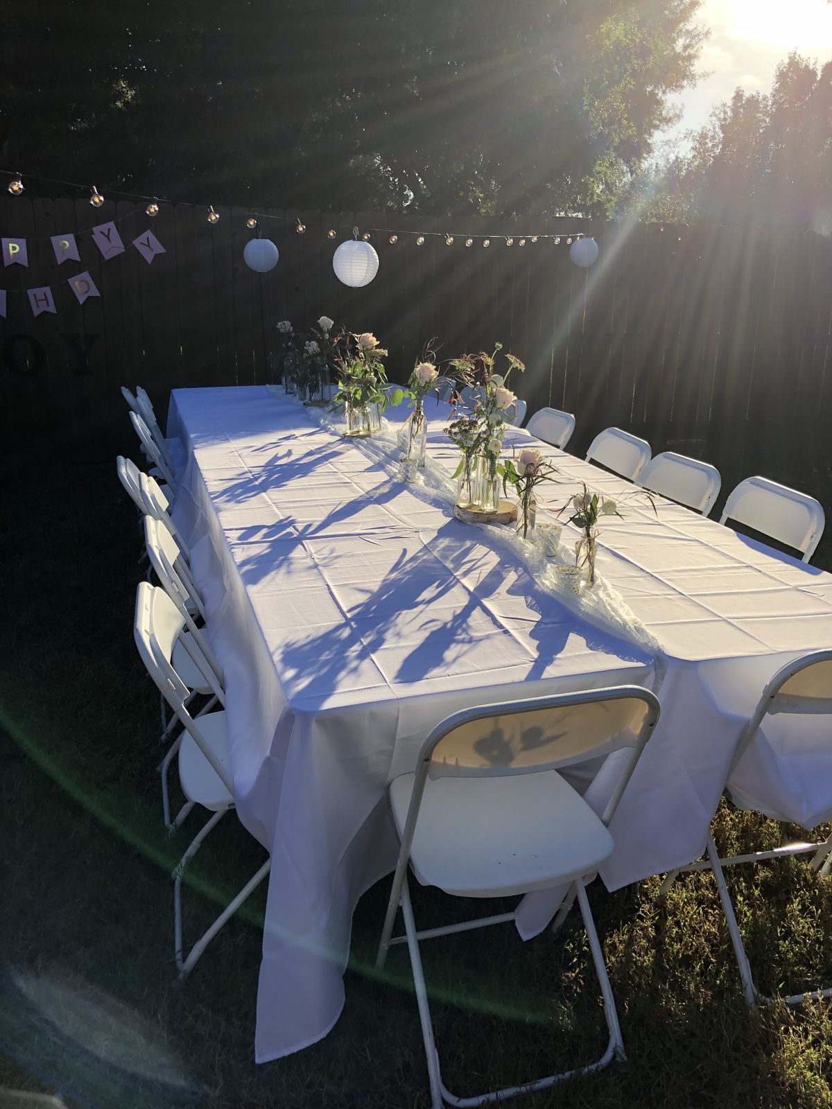 Outdoor celebration dining table with white folding chairs setup by EvenFiestas