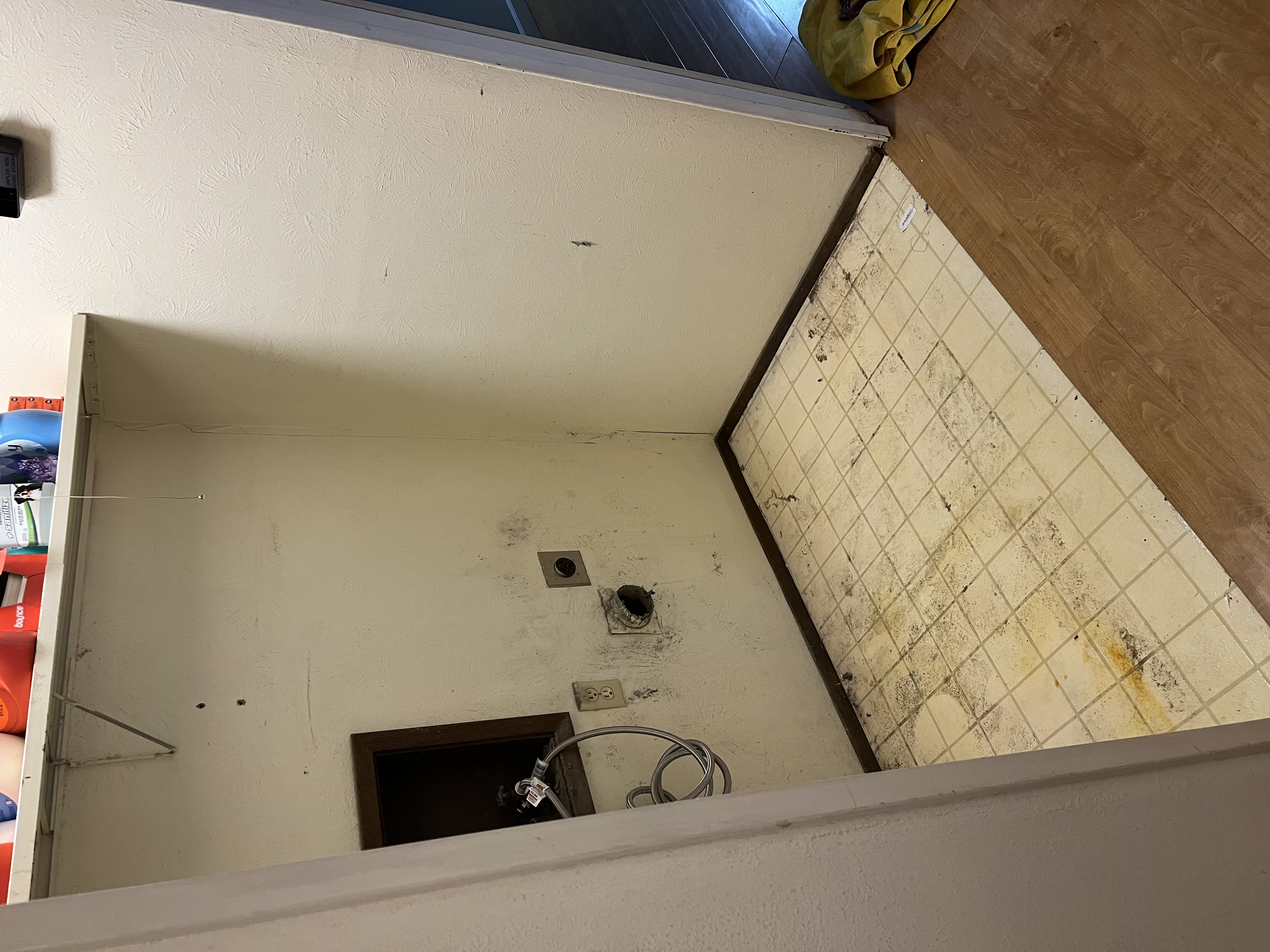 BEFORE: Empty laundry nook with old tile floor, scuffed walls, exposed plumbing/hookups