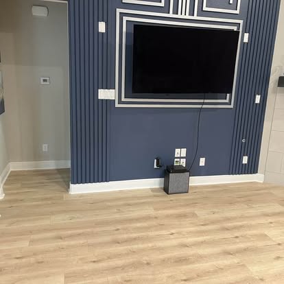 Navy blue accent wall with vertical slat paneling, TV mount, geometric painted border trim, and LVP flooring