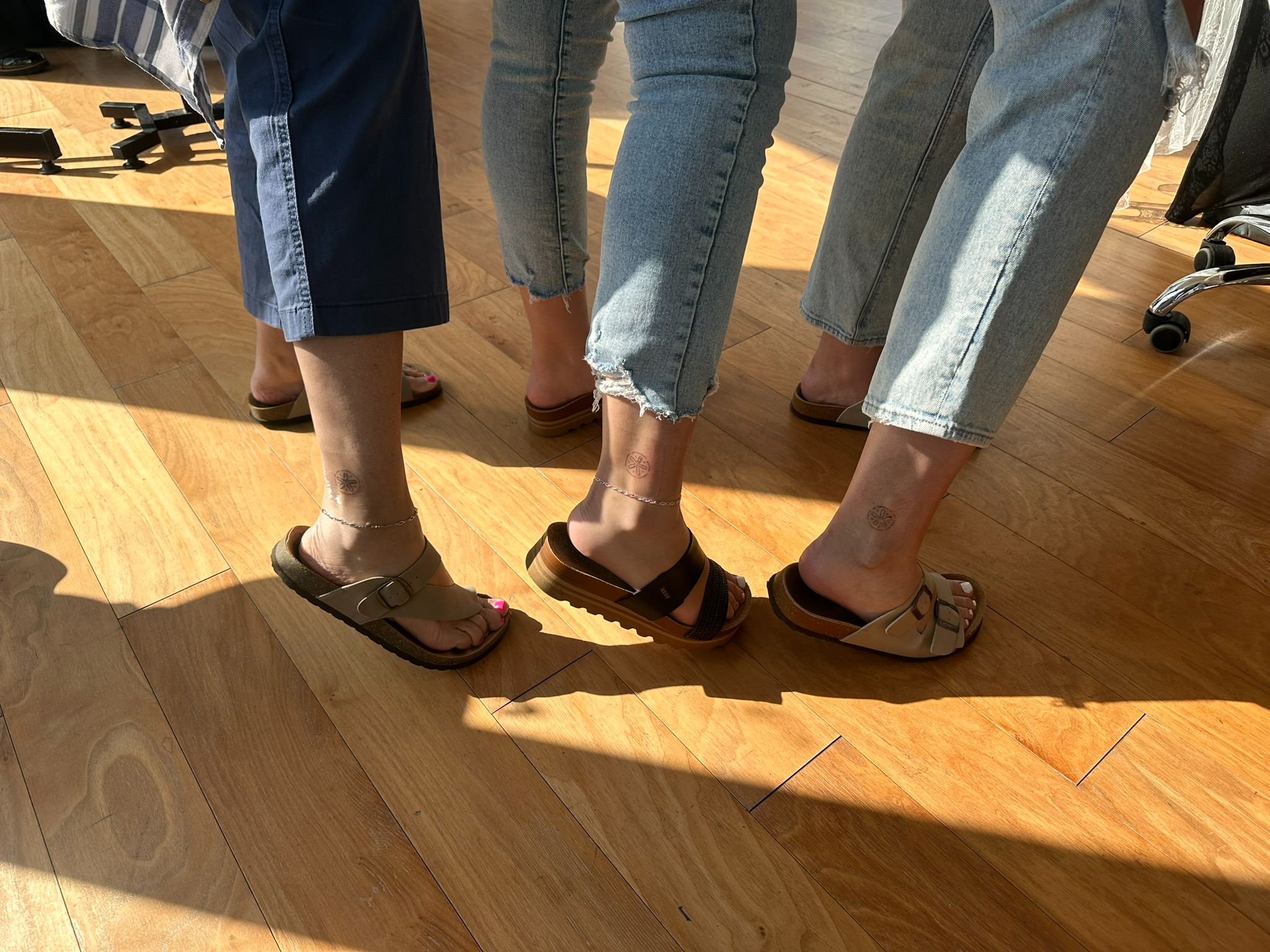 Three guests standing together displaying their matching ankle tattoos