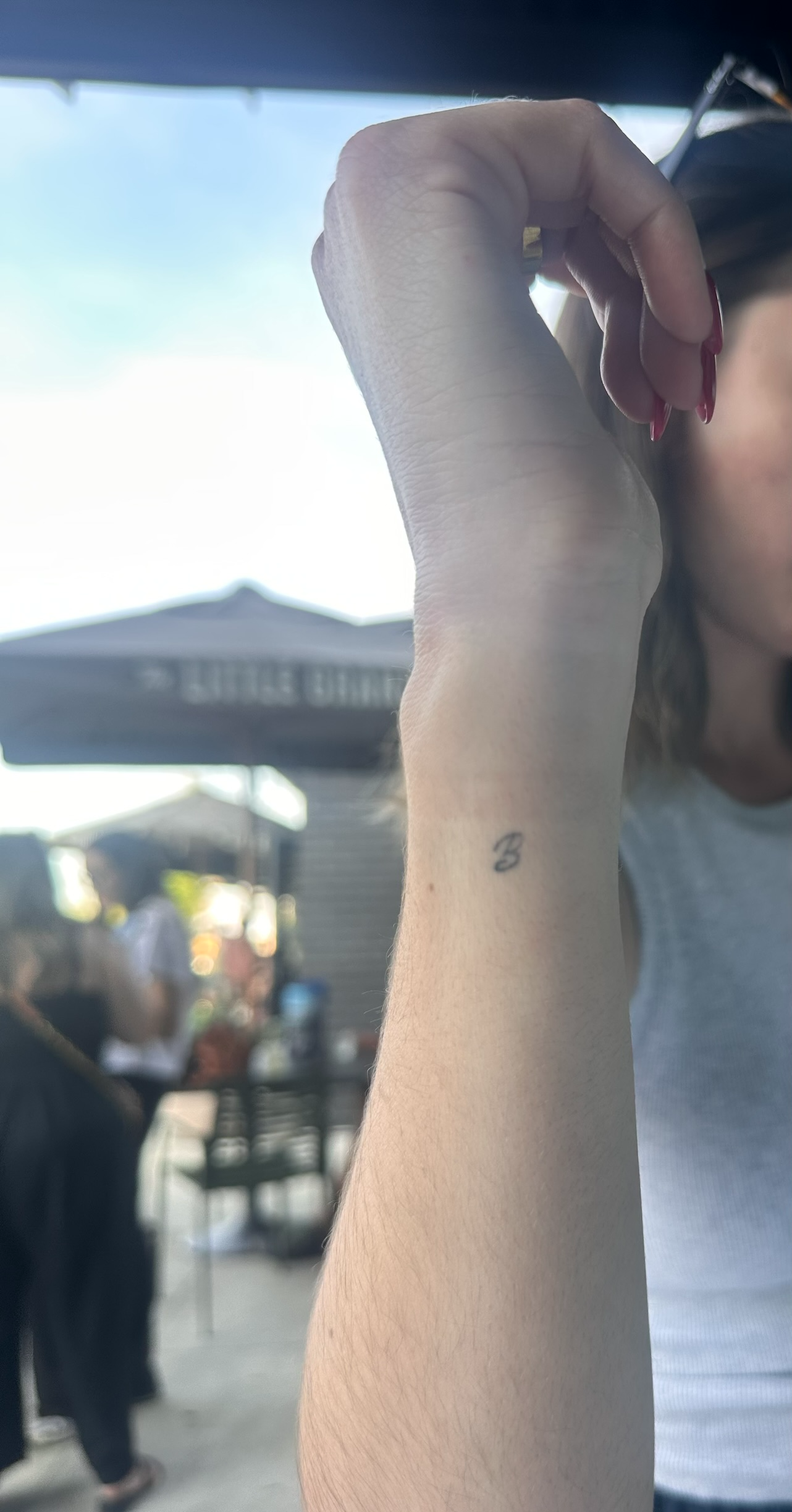 Client showing healed fine line initial tattoo on wrist at outdoor event