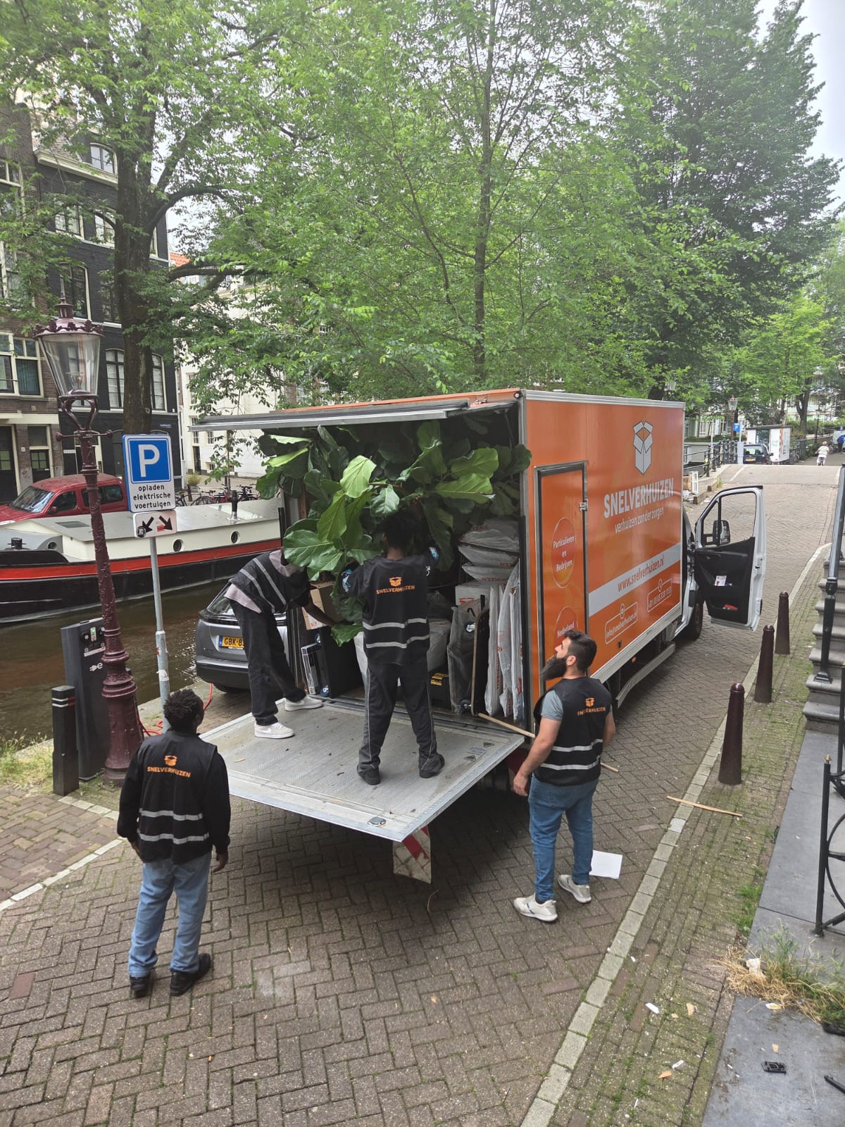 Verhuizers van Snelverhuizen laden inboedel in de verhuiswagen aan een gracht in Amsterdam