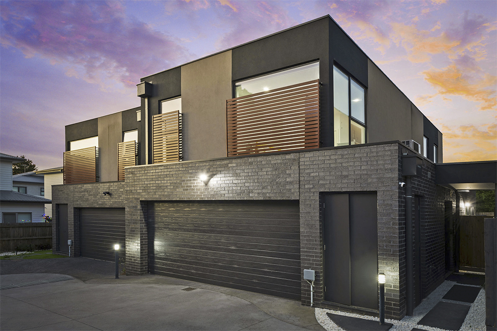 Twilight photography of a contemporary dark brick home with illuminated garage and purple dusk sky