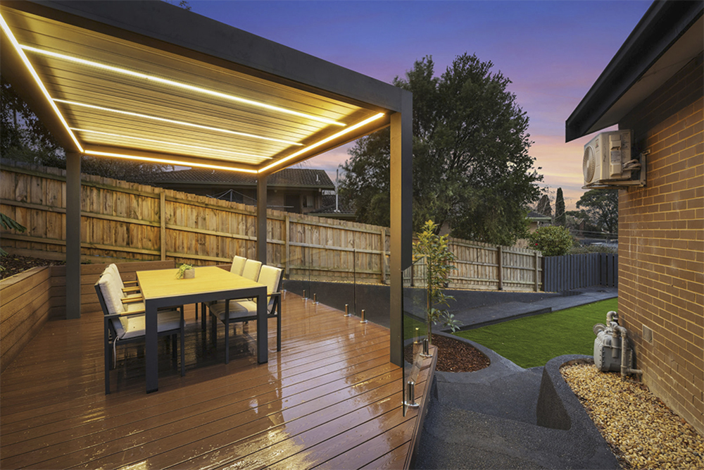 Twilight exterior of a covered deck with LED strip lighting and lush backyard at golden hour