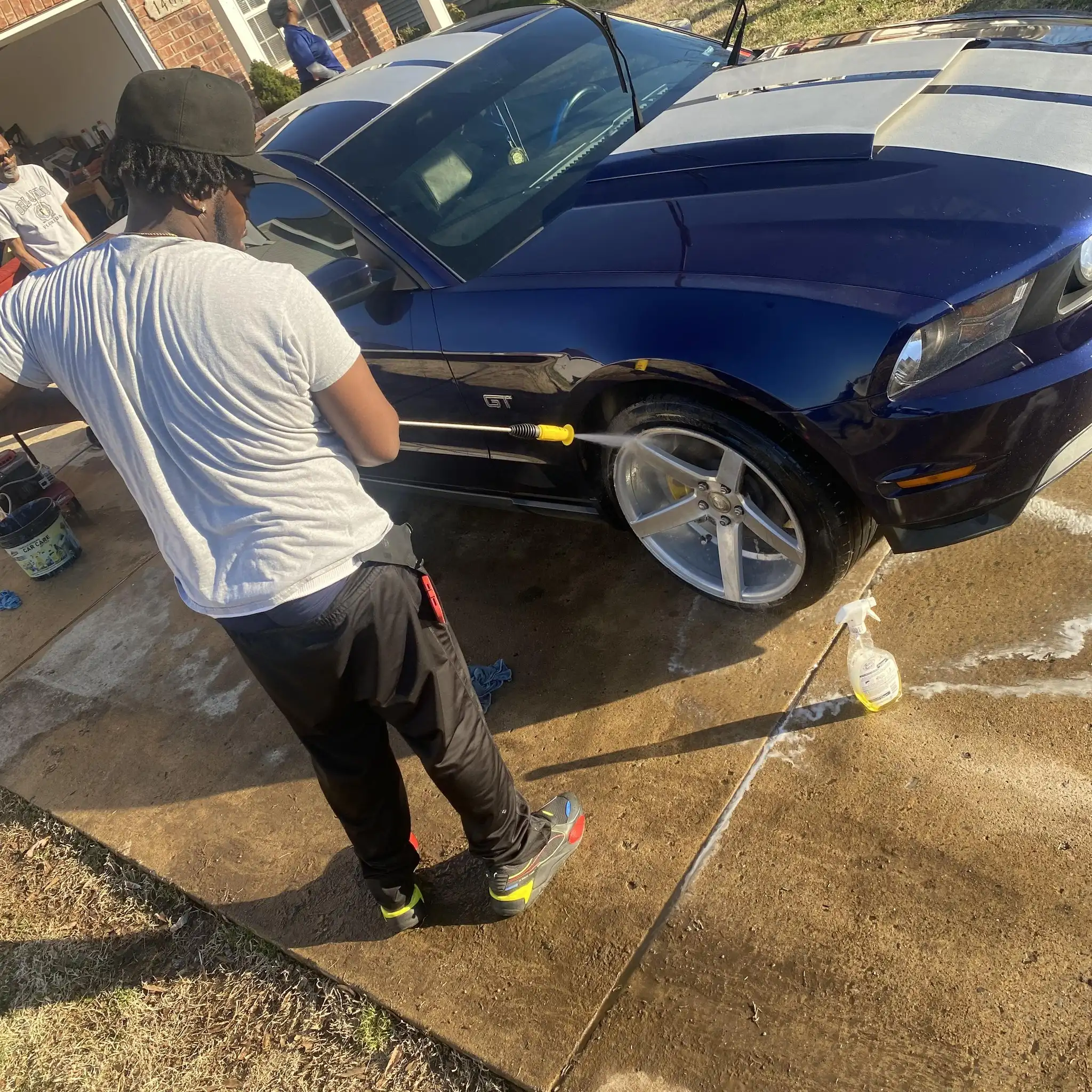 Mobile detailer pressure washing a dark blue Mustang in a residential driveway