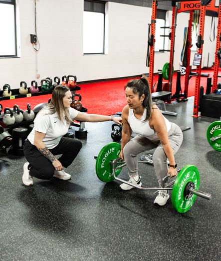 Coach adjusting a member's form, member 50+ performing hex bar deadlift at Results by Design Fitness