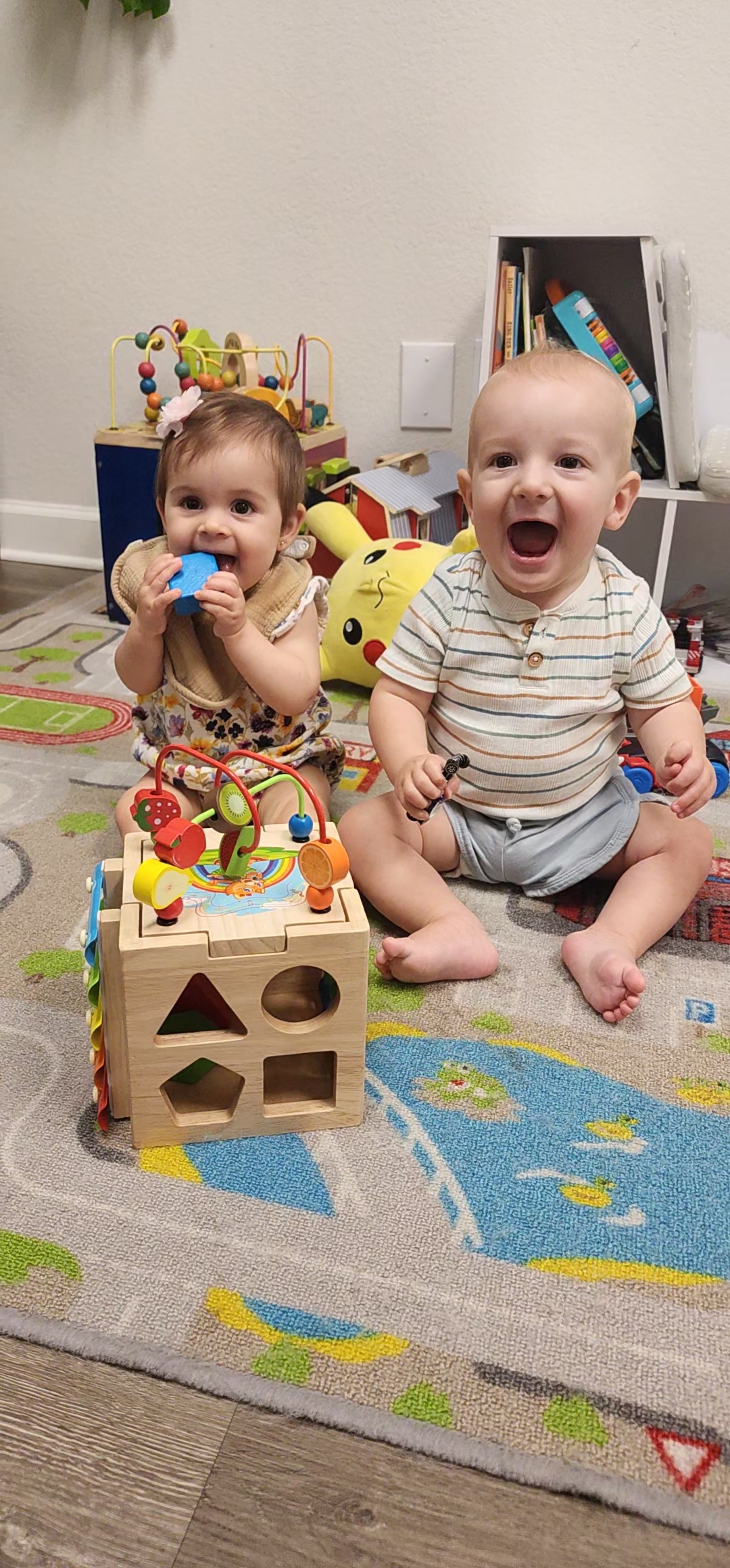 Two happy infants sitting and playing together with toy blocks and shape sorters in a play area at Mojica Chiropractic Care