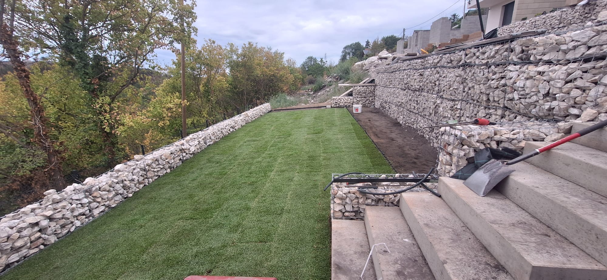 Frissen telepített gyepszőnyeg gabion támfal és kerti lépcső mellett
