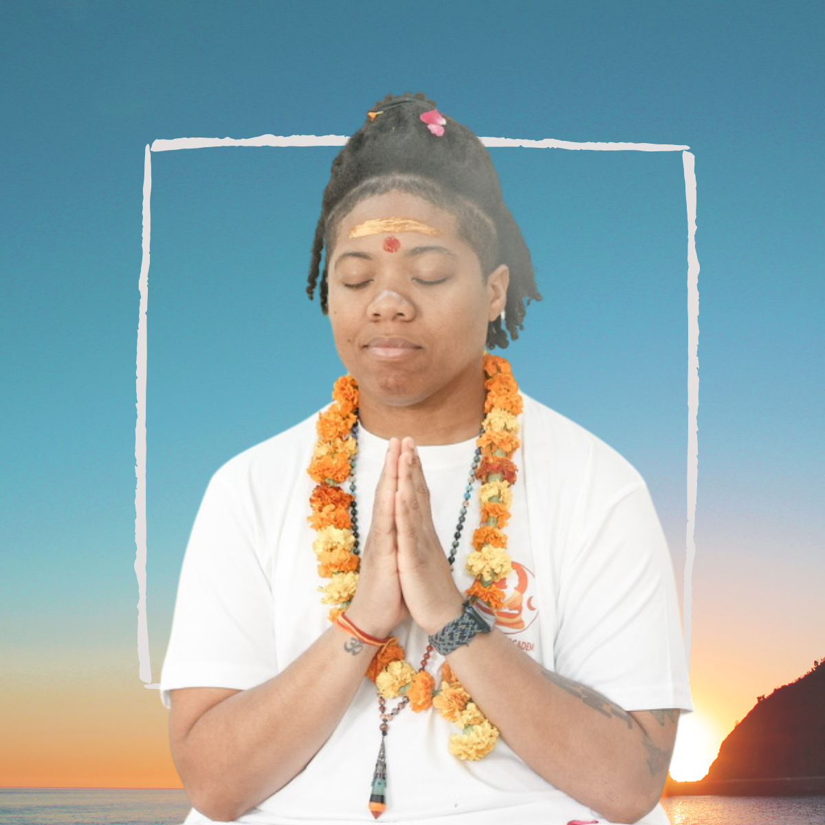 Destinē in seated meditation with hands in prayer and floral garland at sunrise