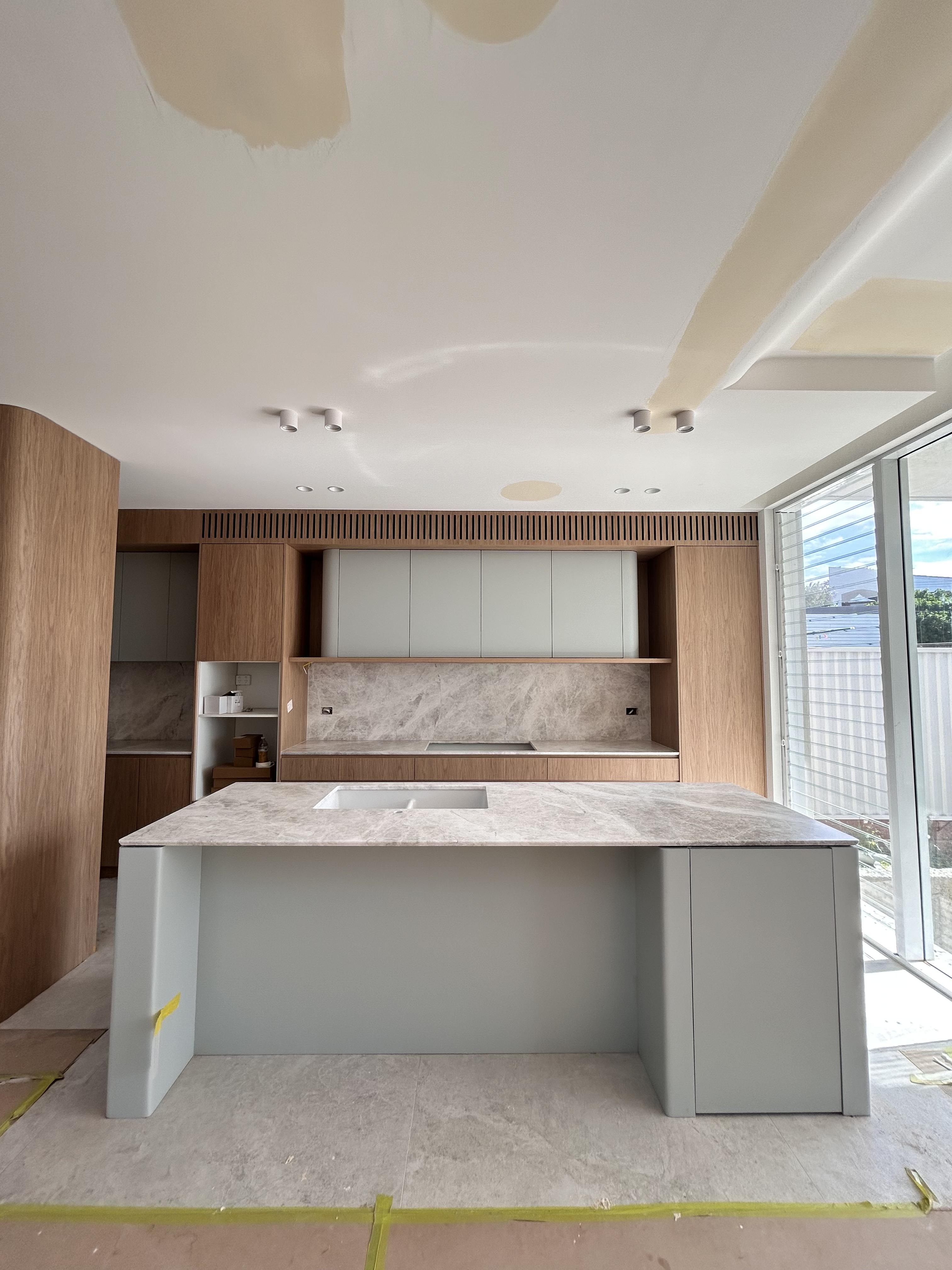 Modern white kitchen with light grey stone island and timber accents, surface protection film applied