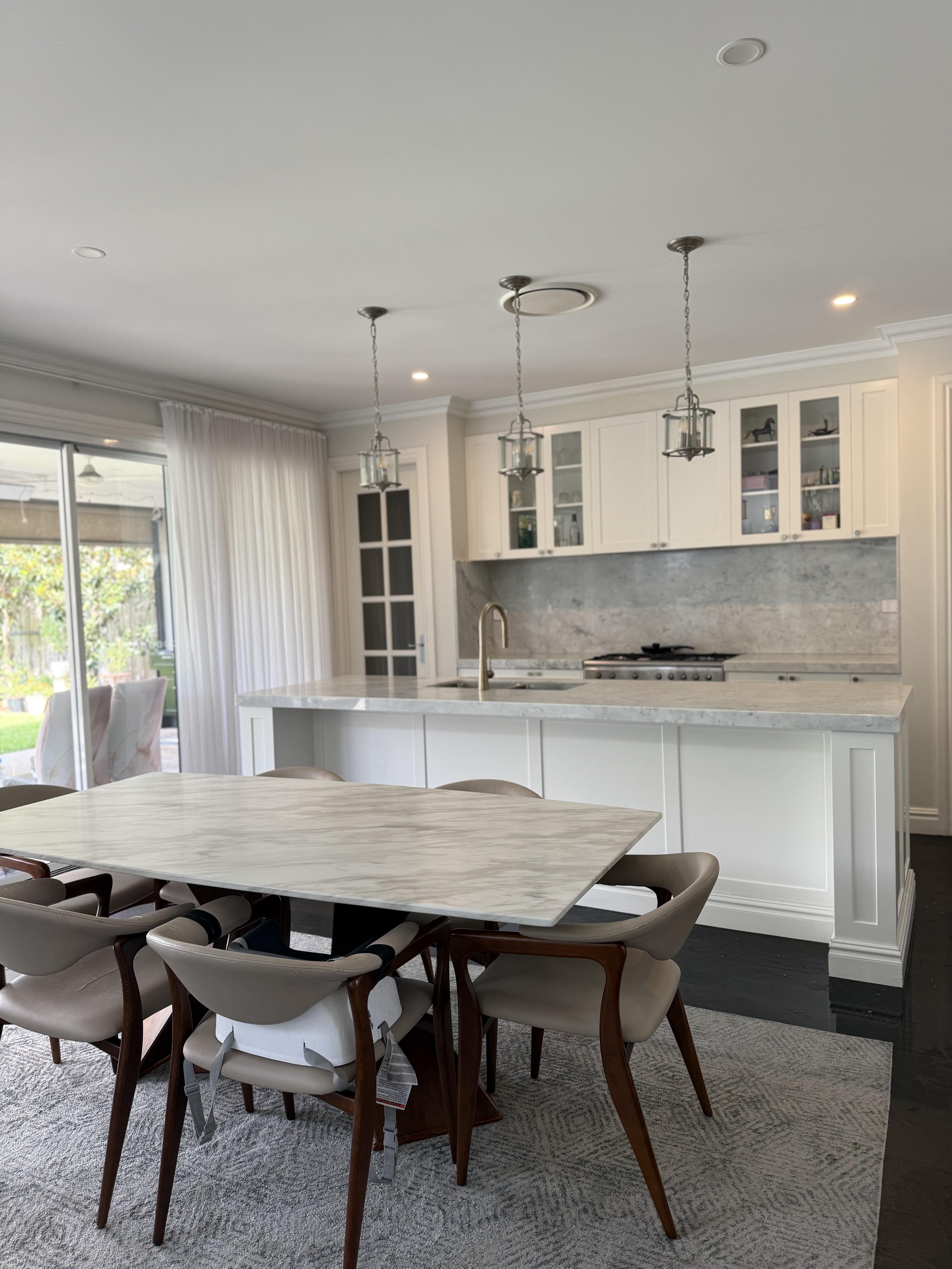 Elegant white open-plan kitchen and marble dining table with pendant lights, stone protection film by Pro Surface Protection