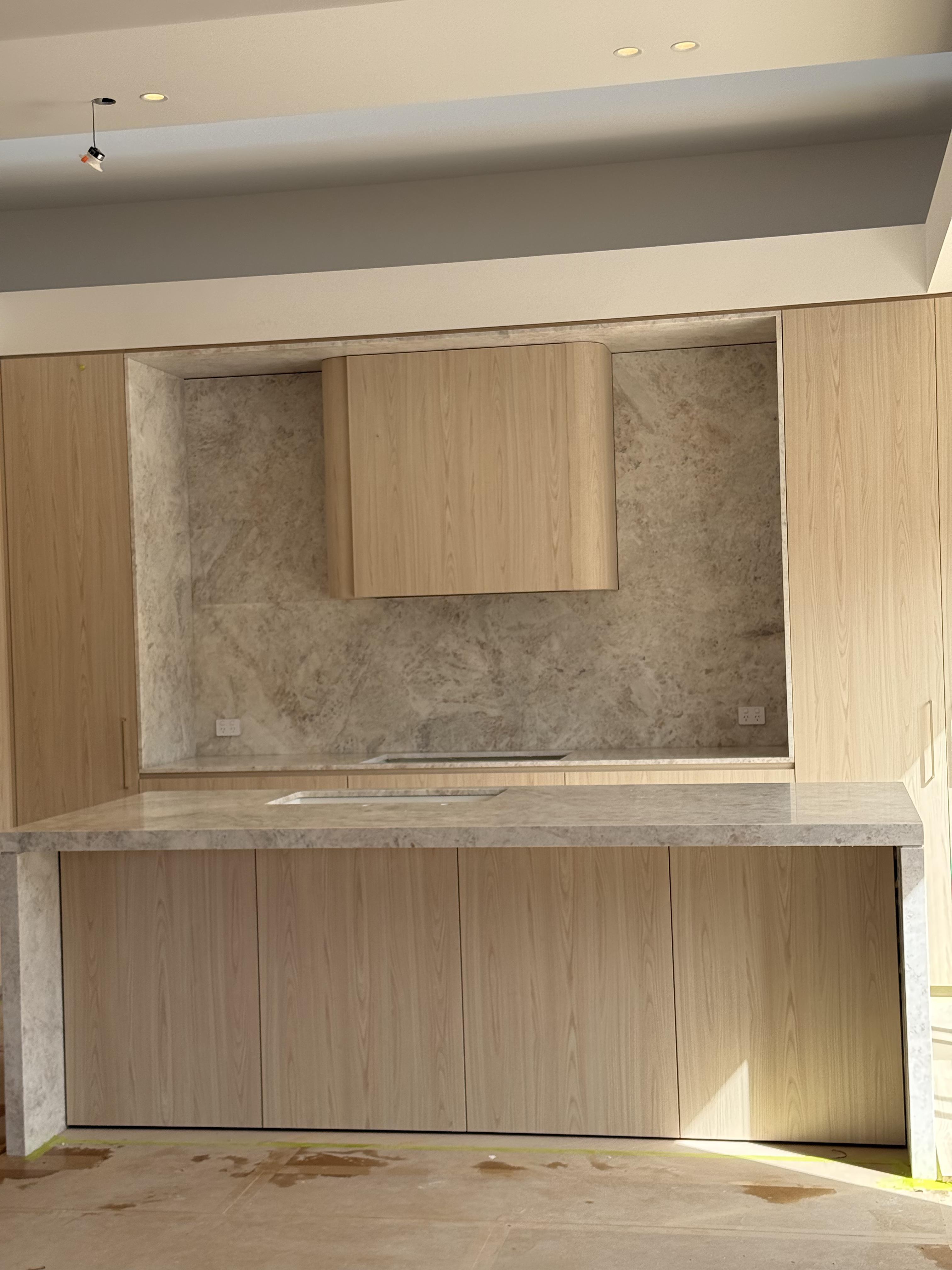 Light timber kitchen cabinets with marble splashback and island protected by surface film