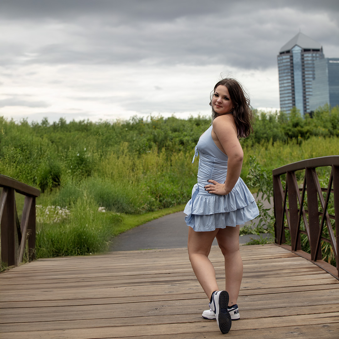 Senior girl posing on a wooden bridge with city buildings in background