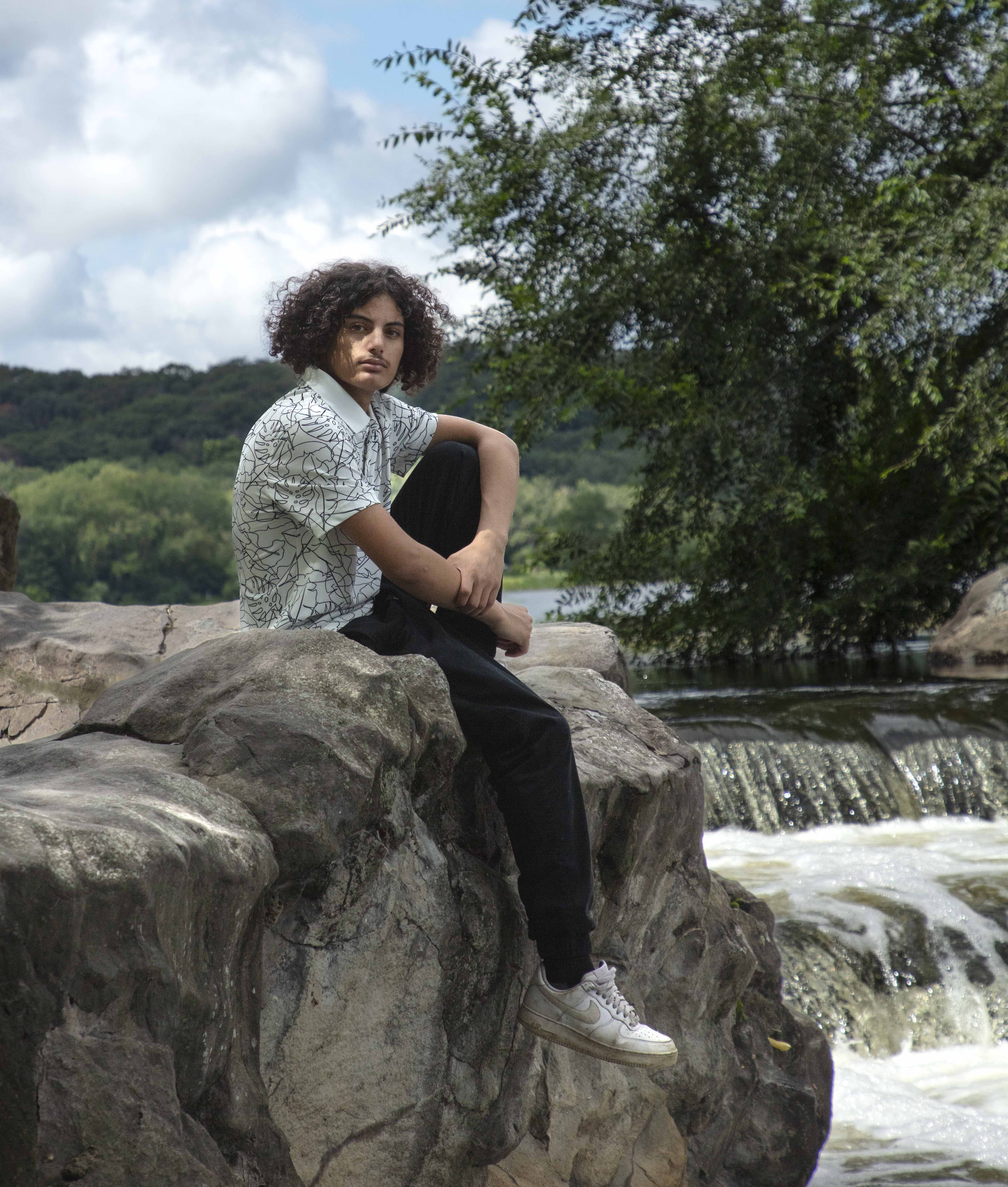 Senior boy sitting on rocks by a waterfall