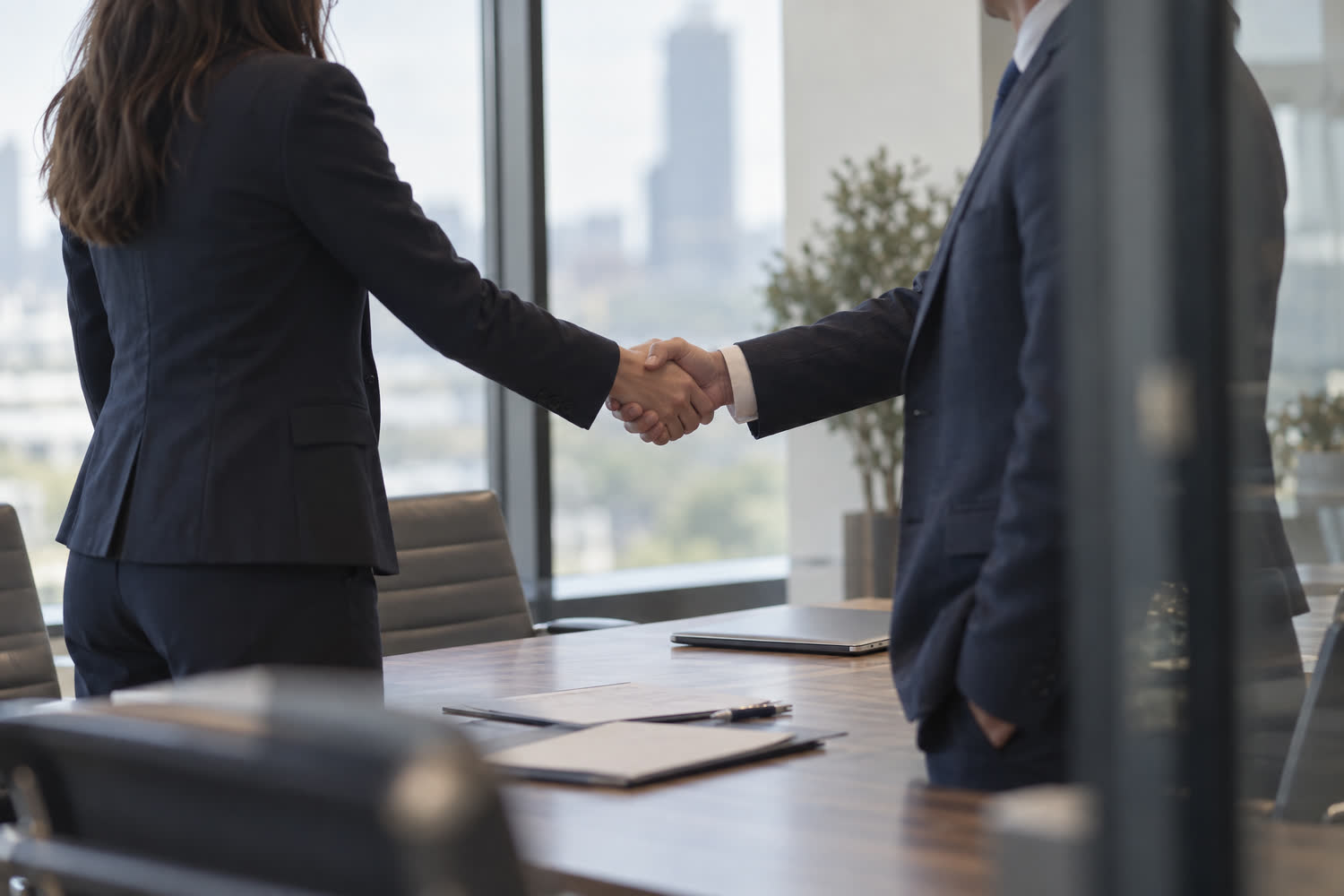 Law firm partners shaking hands on co-counsel agreement across executive conference table