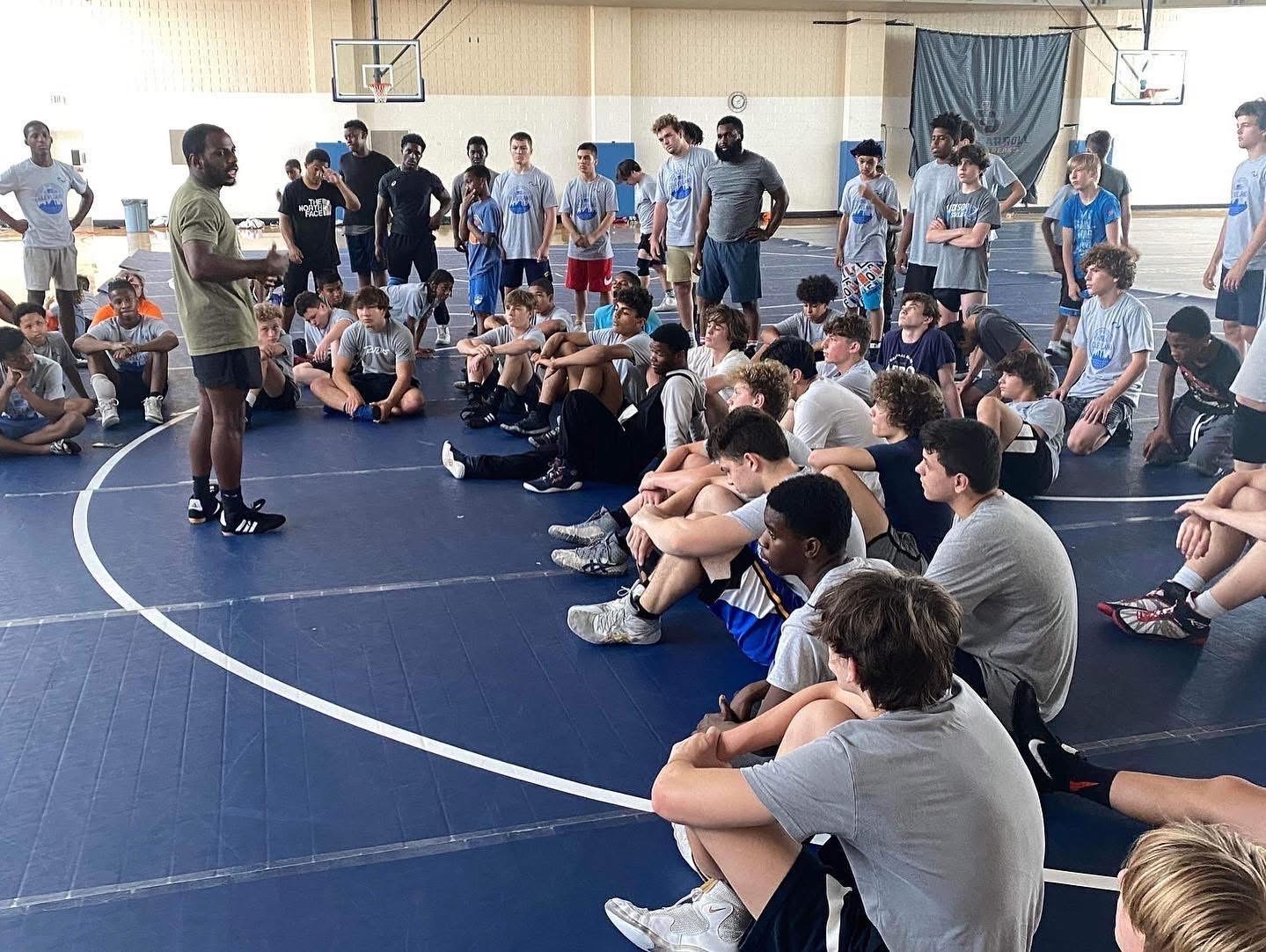 Coach Dee leading a mindset workshop session with athletes on a wrestling mat