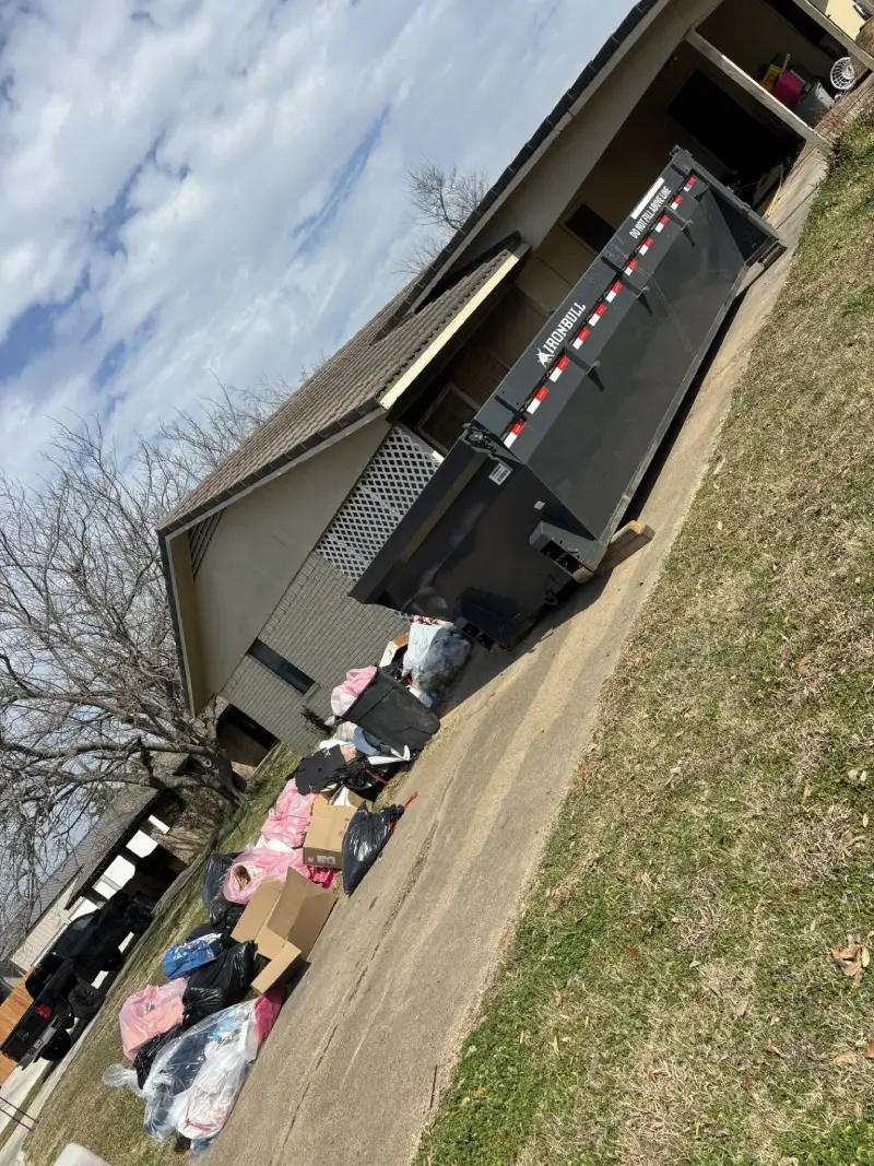 Ironbull roll-off dumpster next to a house with bags of trash