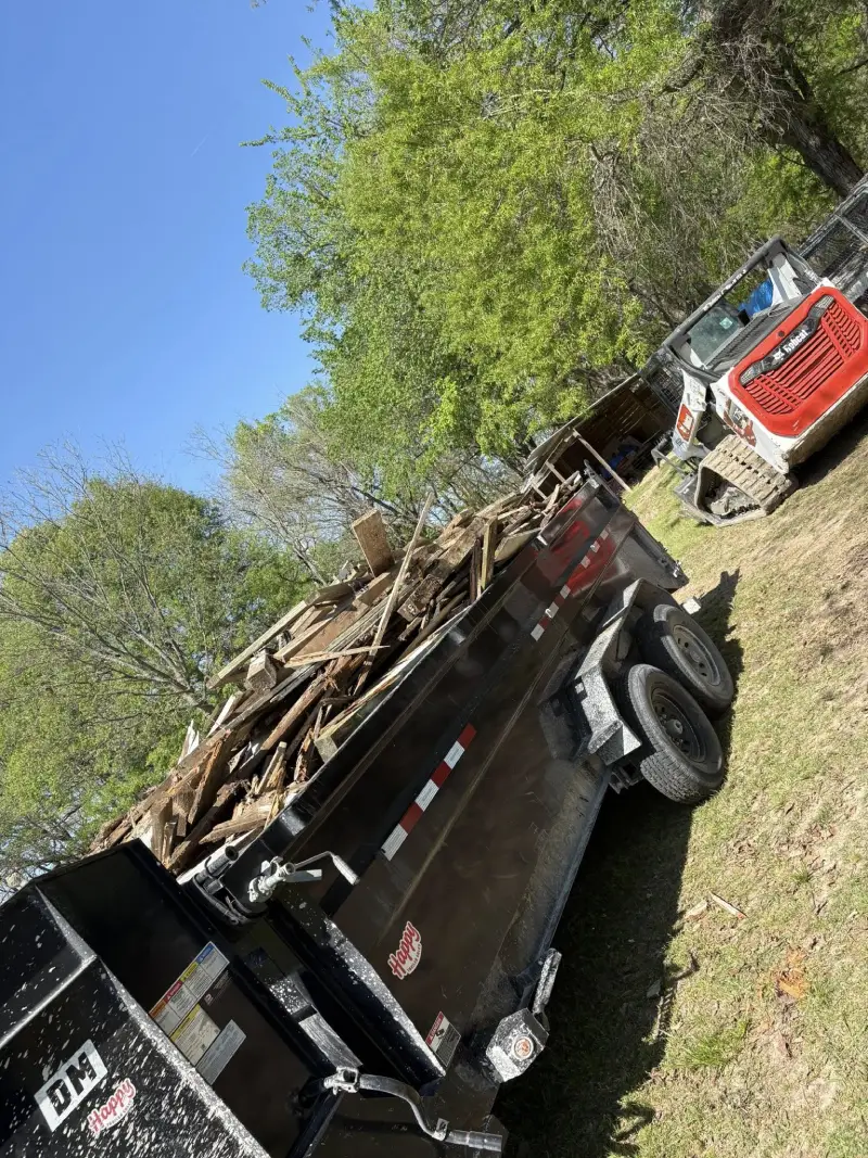 Dump trailer loaded with demolition wood debris next to a bobcat