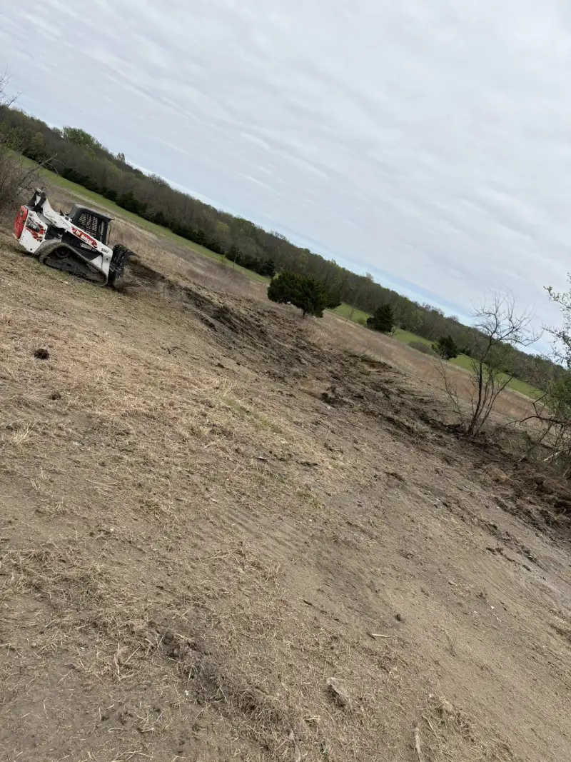 Bobcat skid steer clearing brush and dirt in a field