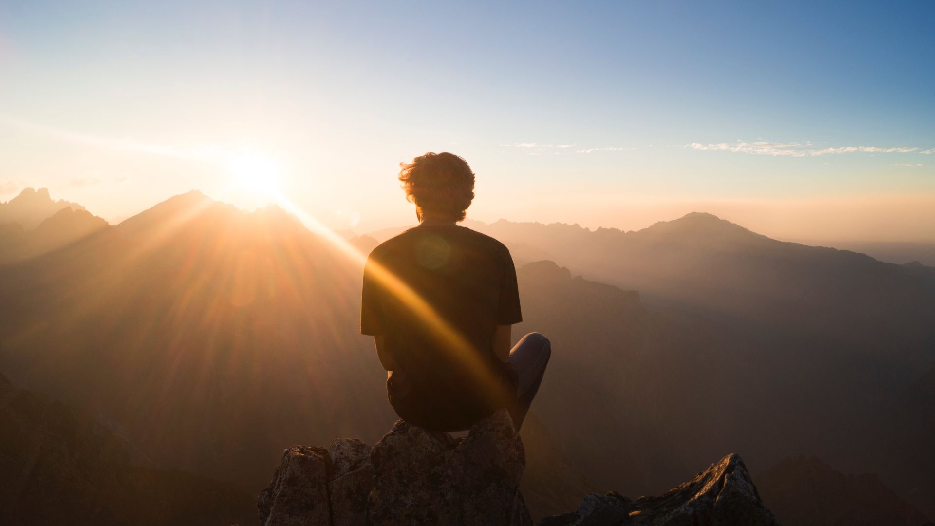 Person sitting on mountain peak at sunrise