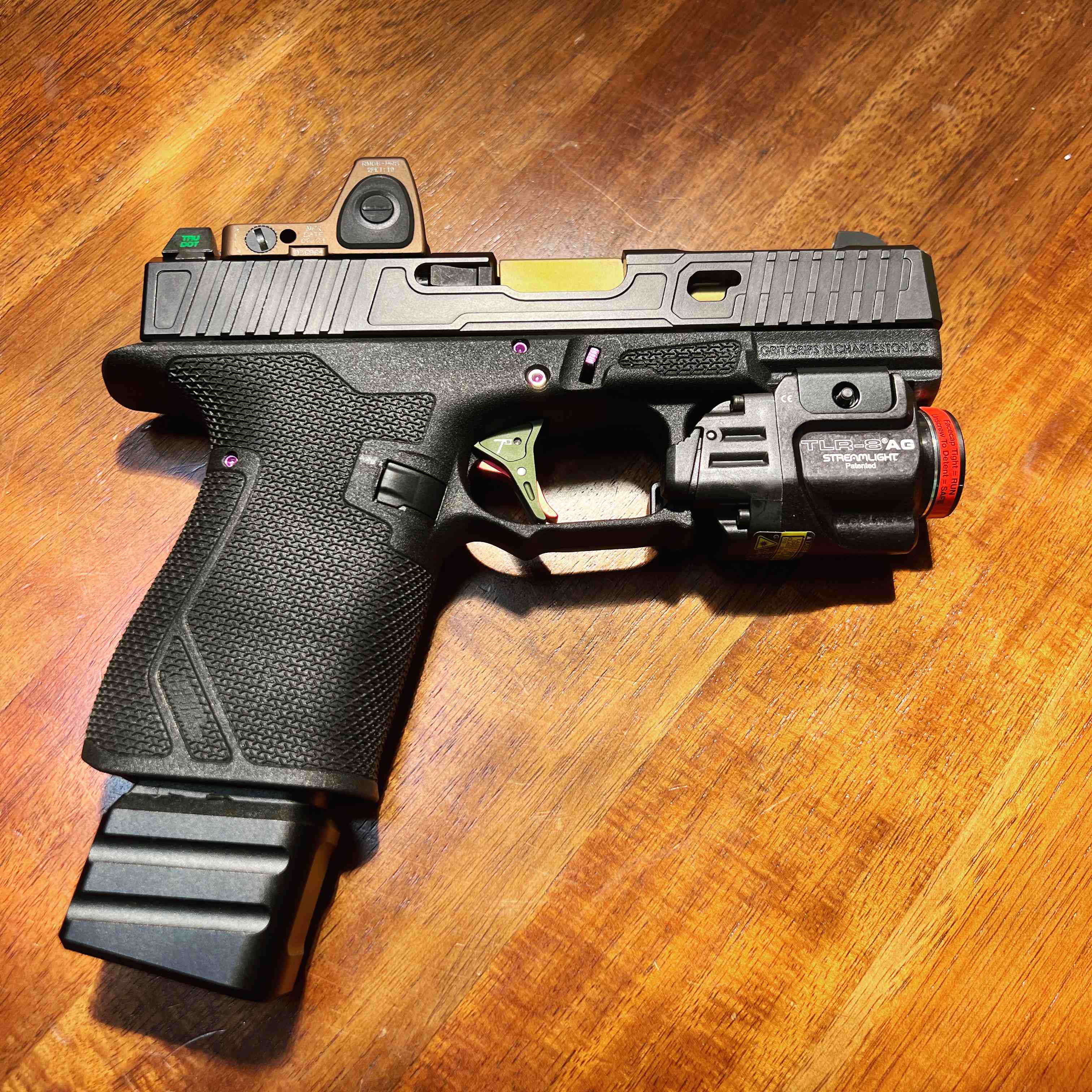 Custom black Precise Arms pistol with optic and mounted light on dark wood
