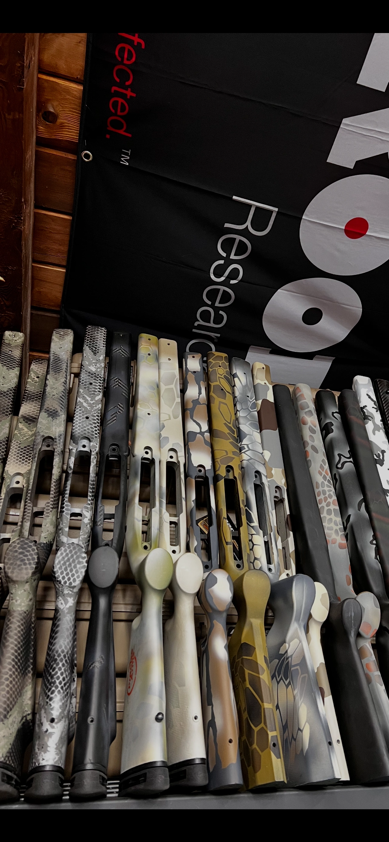 Custom rifle stocks with various camouflage and pattern finishes displayed in a workshop row.