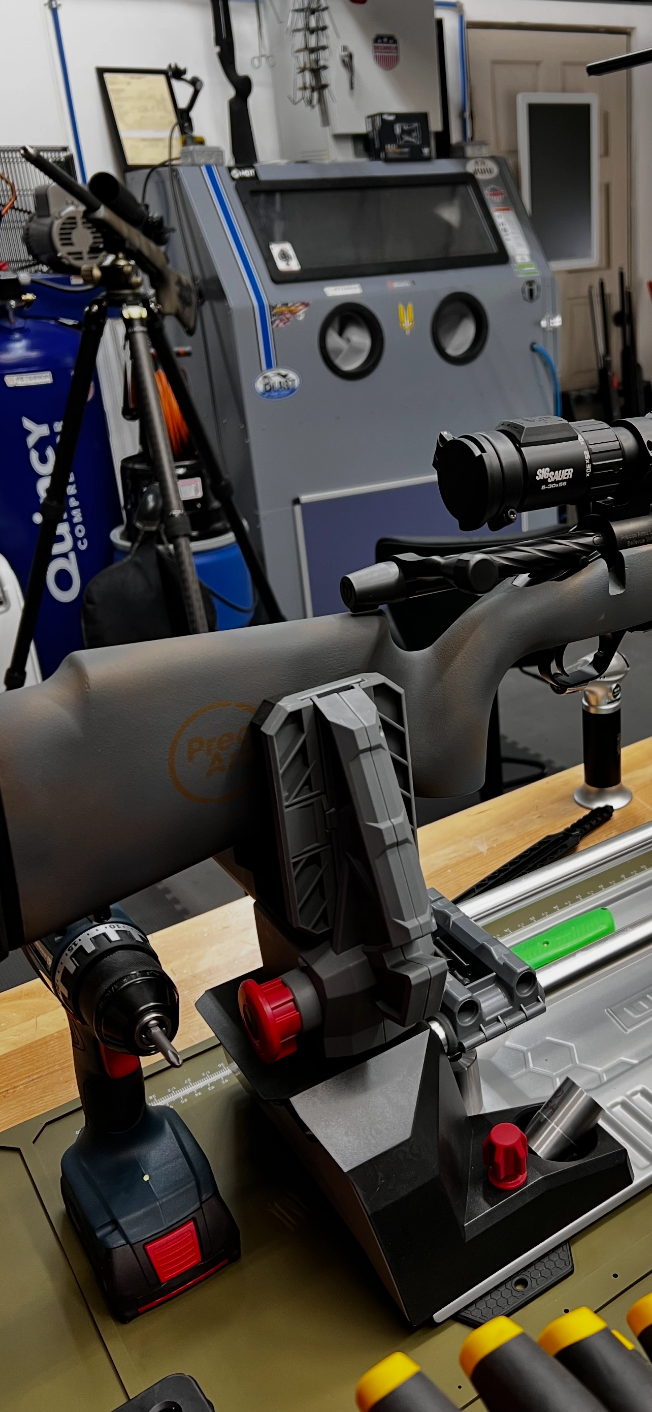 Custom rifle mounted in a workbench vise with blast cabinet and workshop equipment at Precise Arms