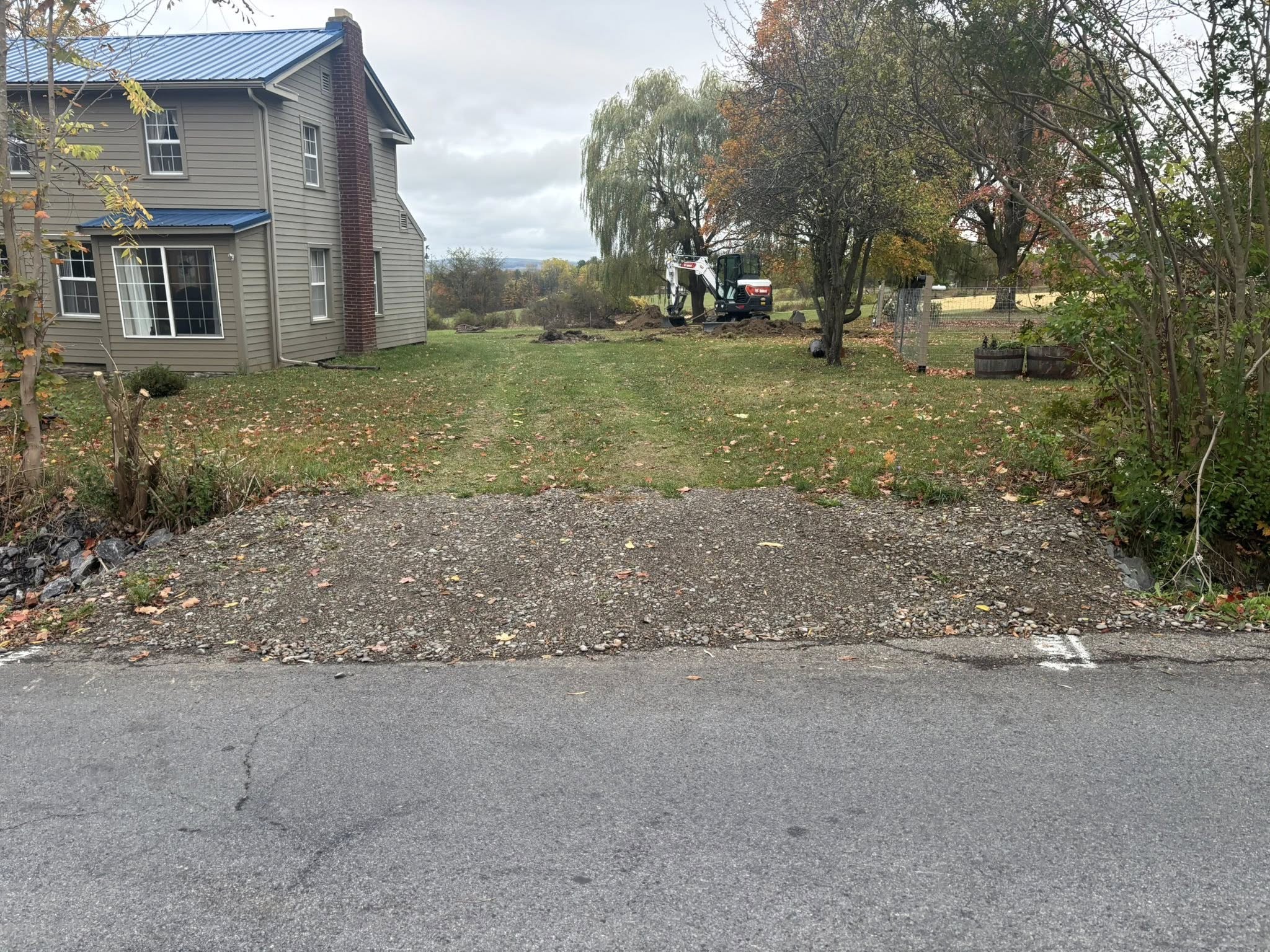 Gravel driveway entrance with house and mini excavator in background