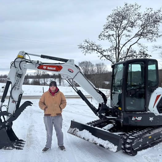 Owner Joe standing next to his Bobcat mini excavator in the snow