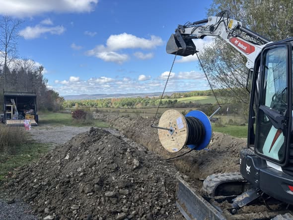 Mini excavator lifting a spool of cable for trenching