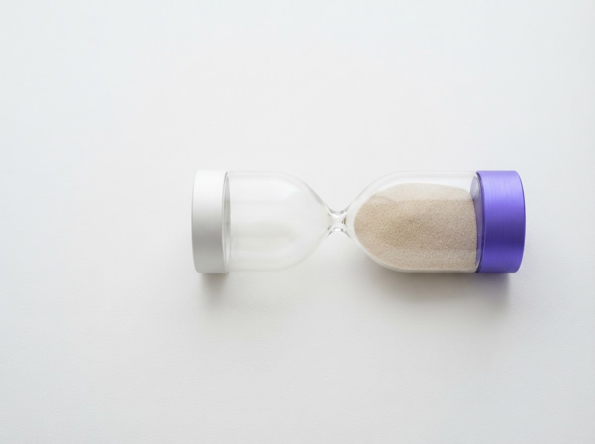 An hourglass laid on its side on a white surface with the sand settled and still, one violet base cap