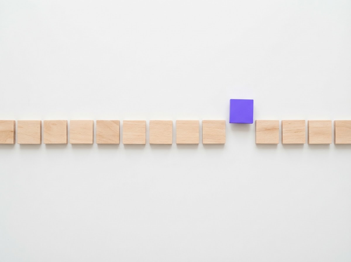 Pale wooden tiles laid out in a neat row on white, one violet tile lifted slightly out of line as though being selected