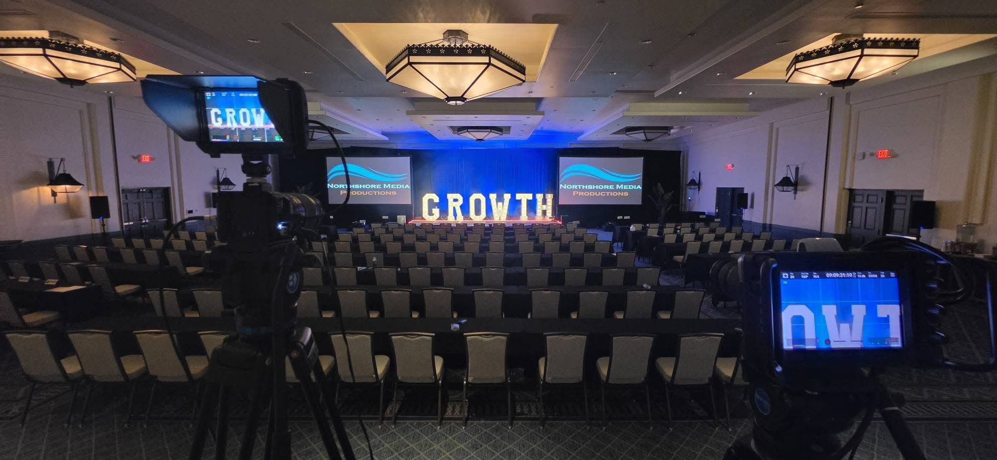 Company-owned growth conference ballroom stage with broadcast camera and full seating