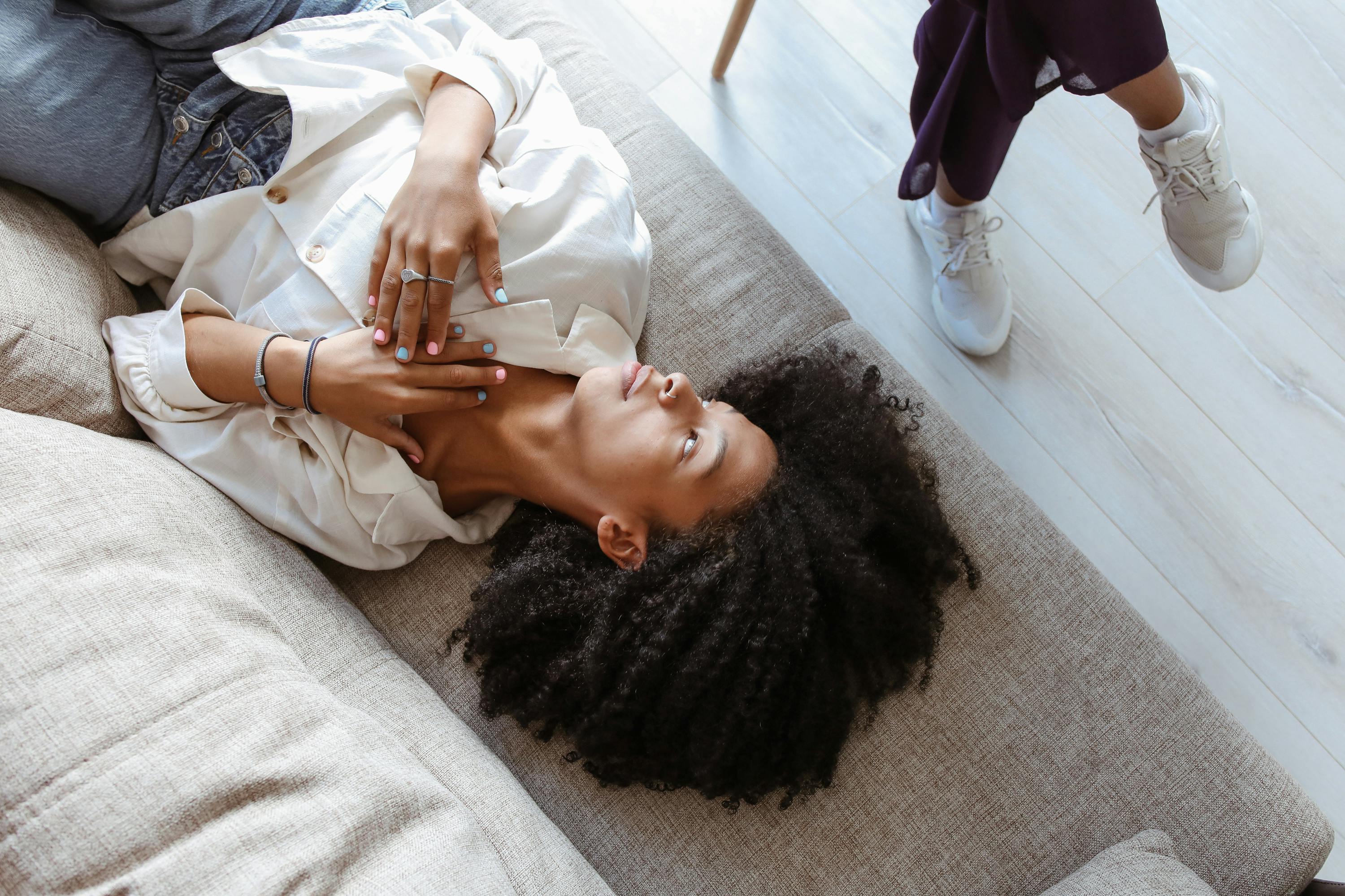 Woman lying on a couch with hands on chest, showcasing a relaxed demeanor, in a setting that conveys comfort and support, relevant to EMDR therapy for trauma and PTSD at Well Health Counselling.