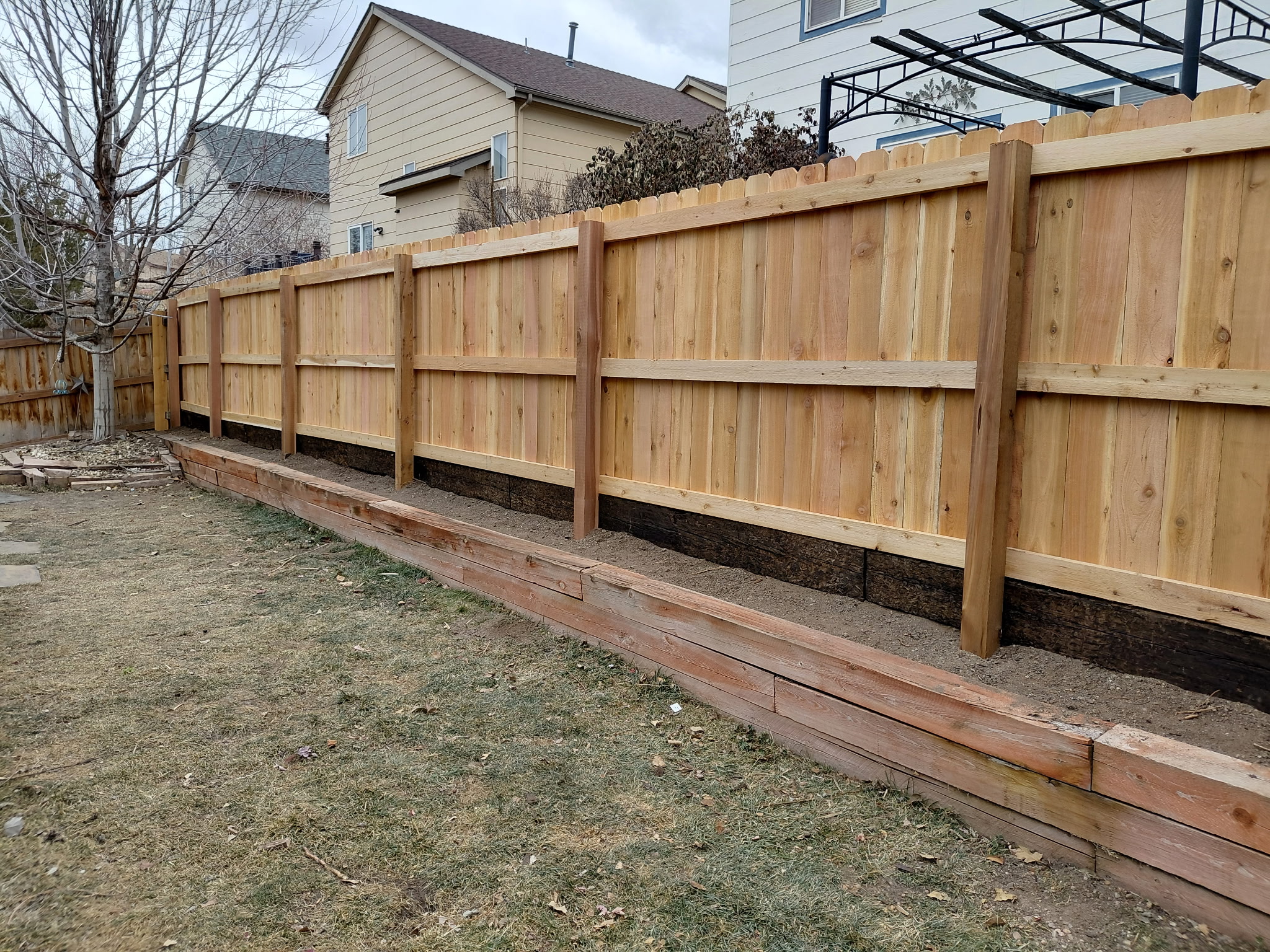 Cedar privacy fence construction with timber retaining wall foundation in Parker, Colorado backyard